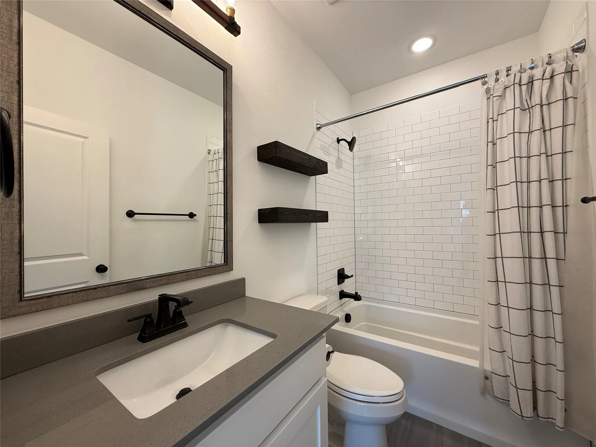 Bathroom featuring a vanity with a solid-surface countertop, rectangular undermount sink, matte black hardware, white subway tile shower surround, and built-in floating shelves