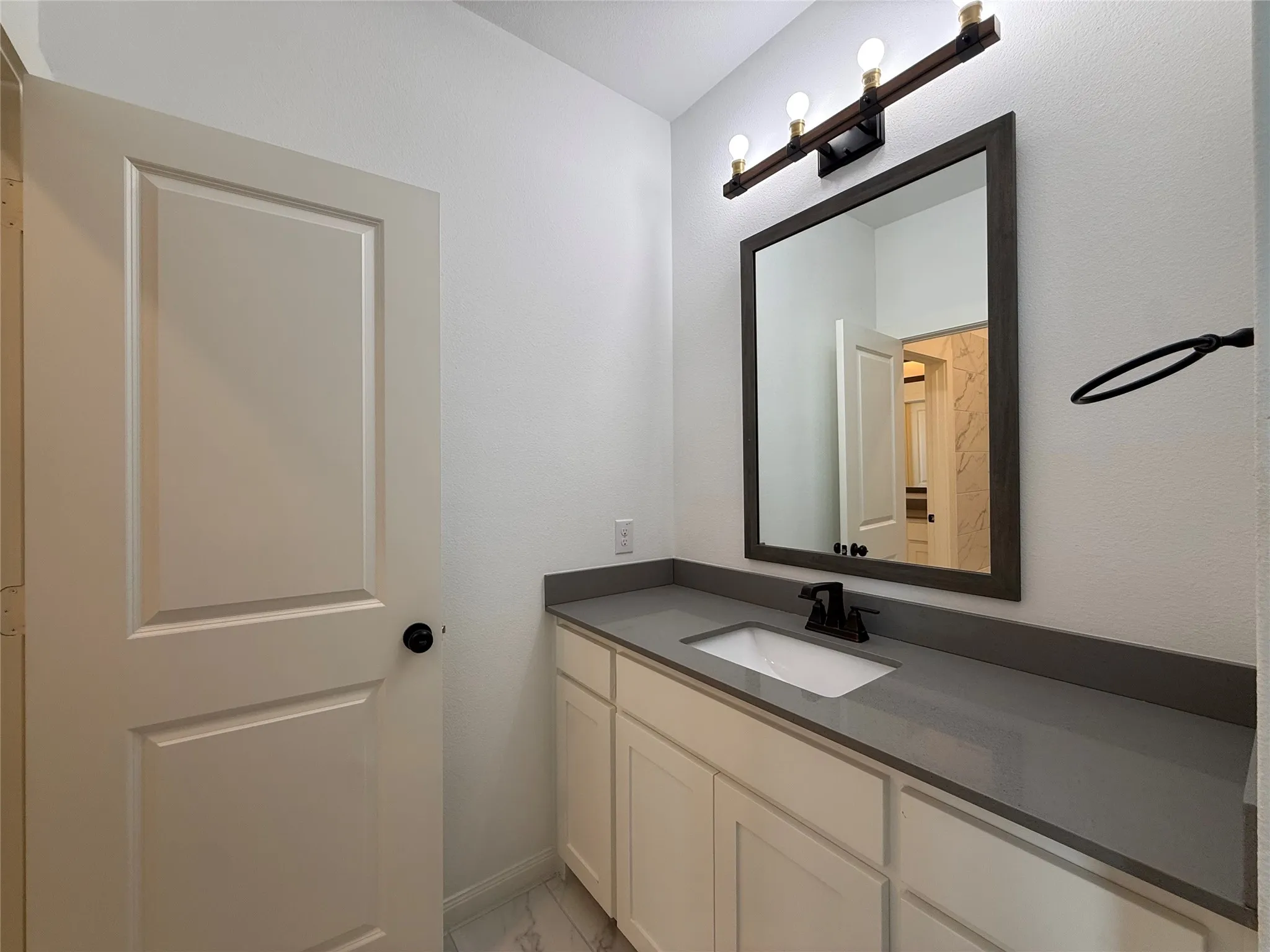 Bathroom vanity featuring shaker-style cabinetry, quartz countertop, undermount sink, dark-finish faucet, and a wall-mounted light fixture