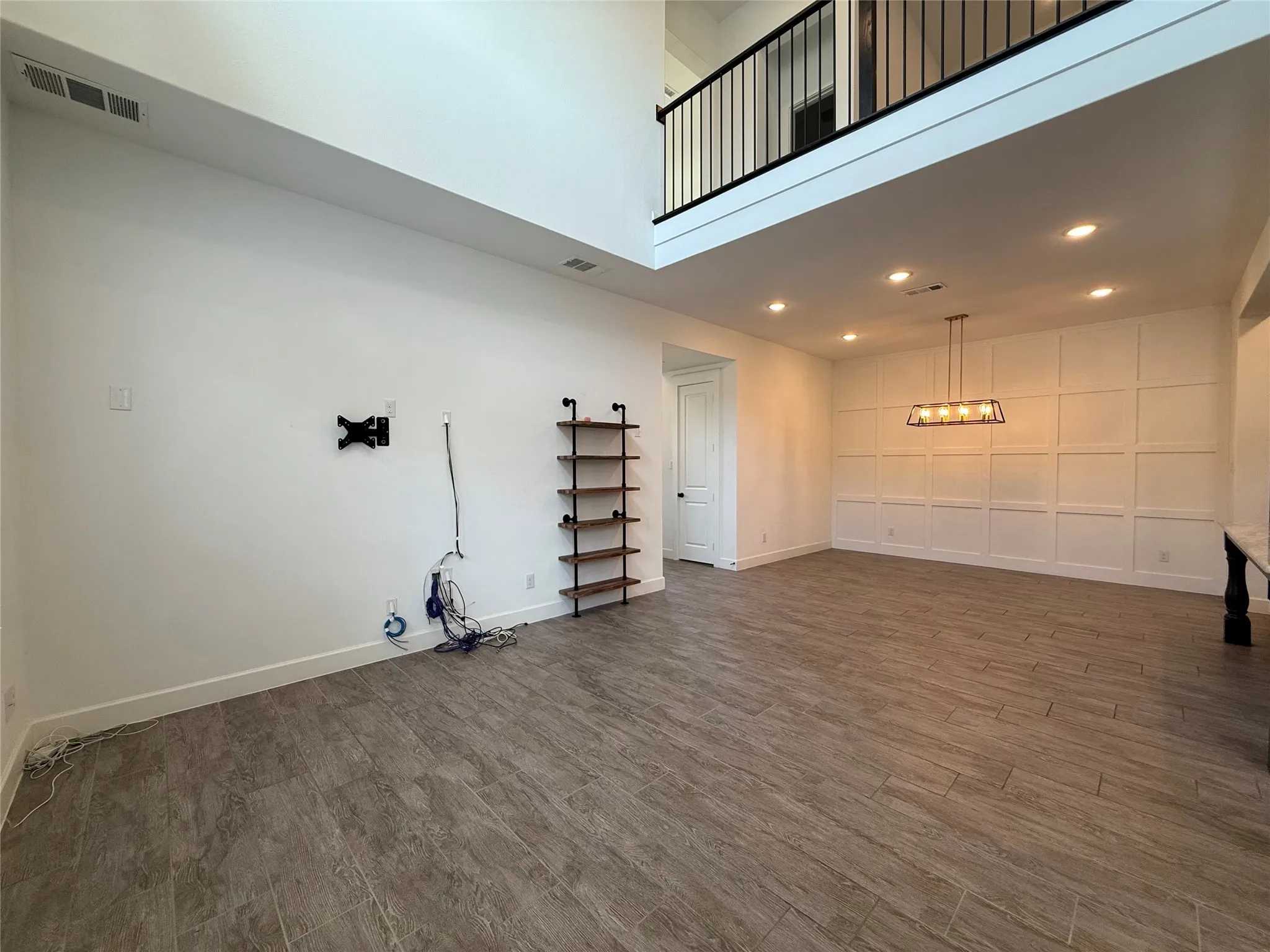 Two-story ceiling height, wood-finish flooring, grid-pattern wall molding, recessed lighting, and metal spindle railing