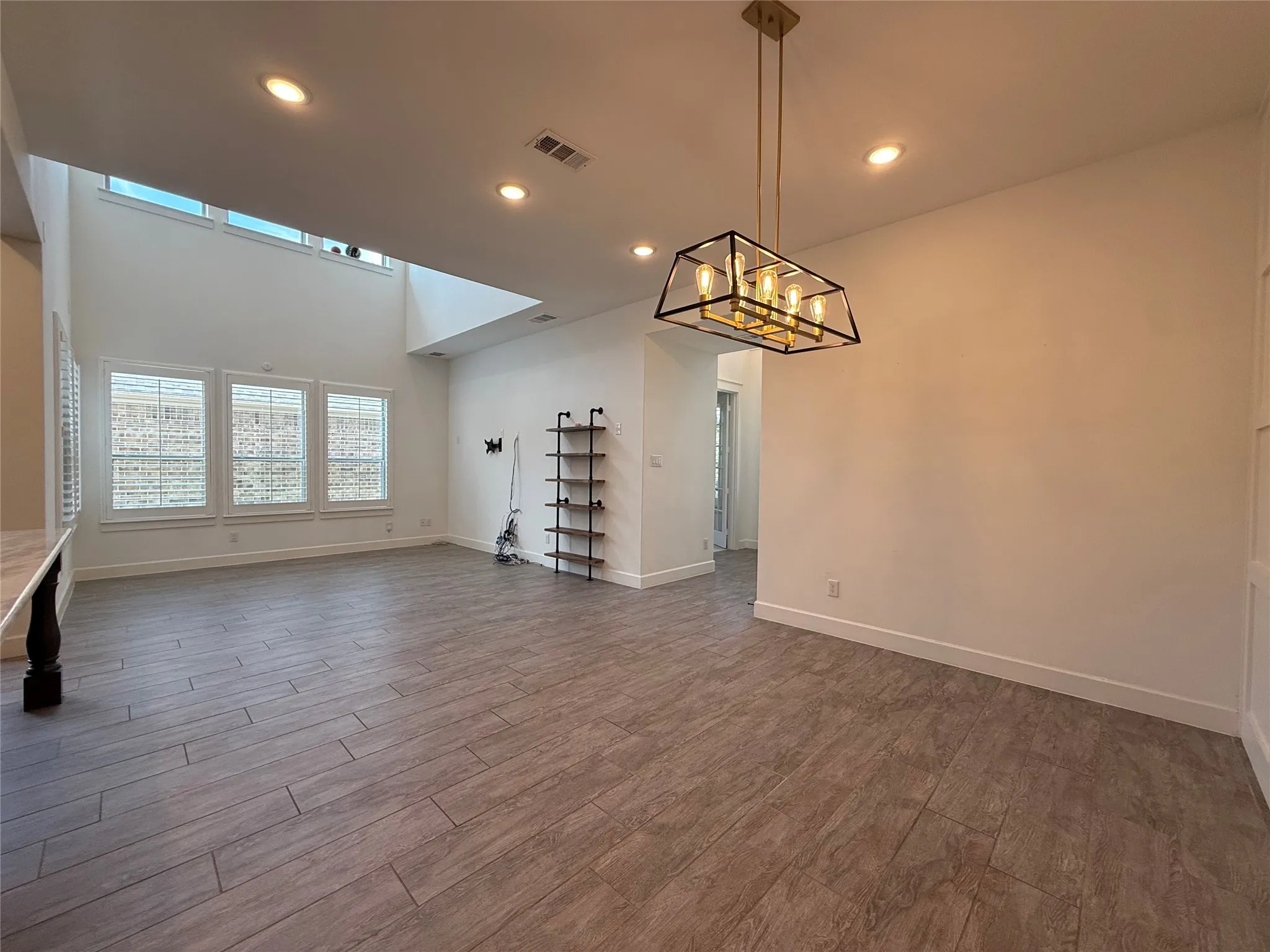 Open-concept space featuring double-height ceilings, wood-finish tile flooring, recessed lighting, and a geometric-frame pendant light fixture