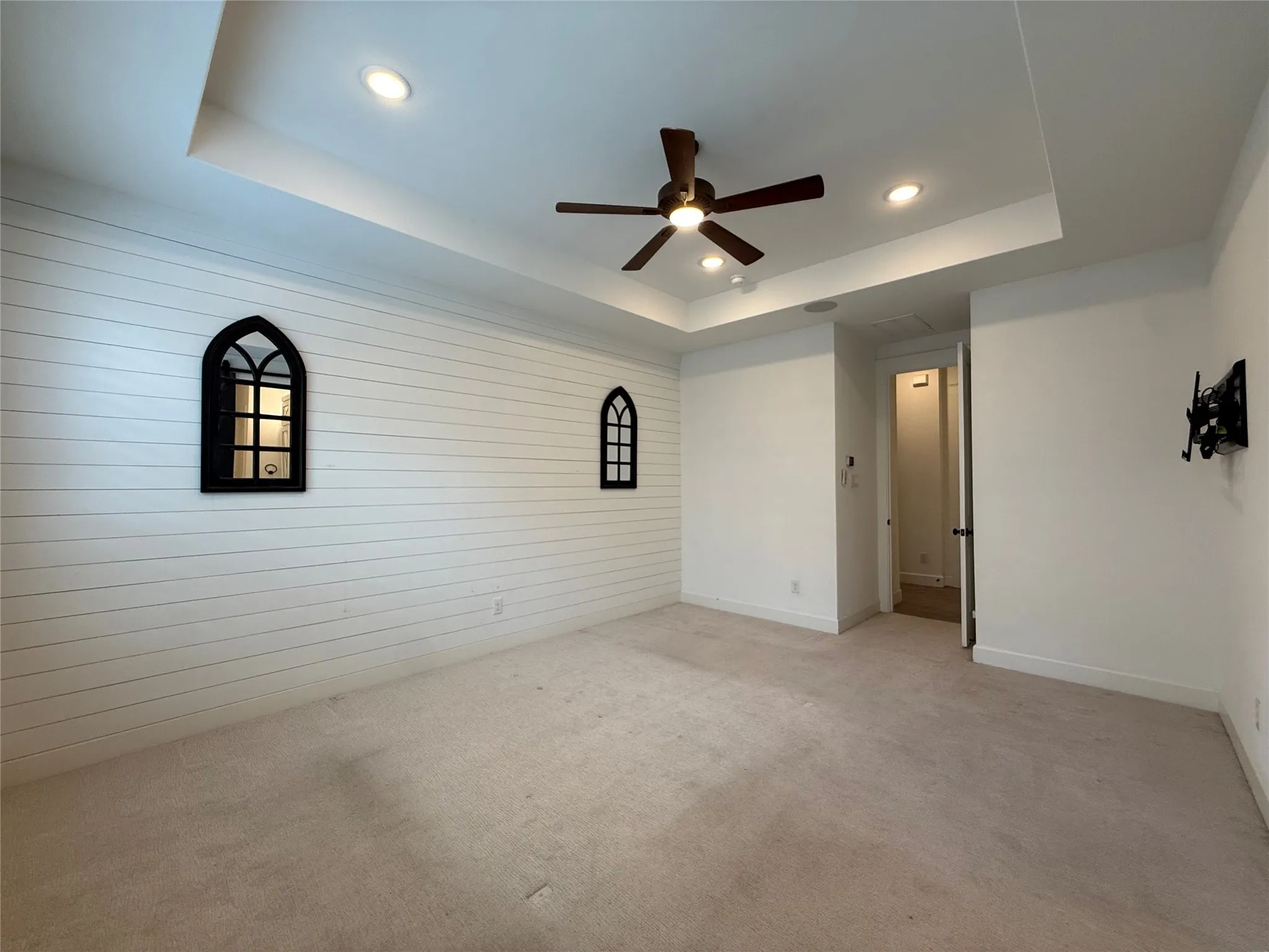 Tray ceiling with recessed lighting, shiplap accent wall, twin arched decorative wall fixtures, and integrated ceiling fan