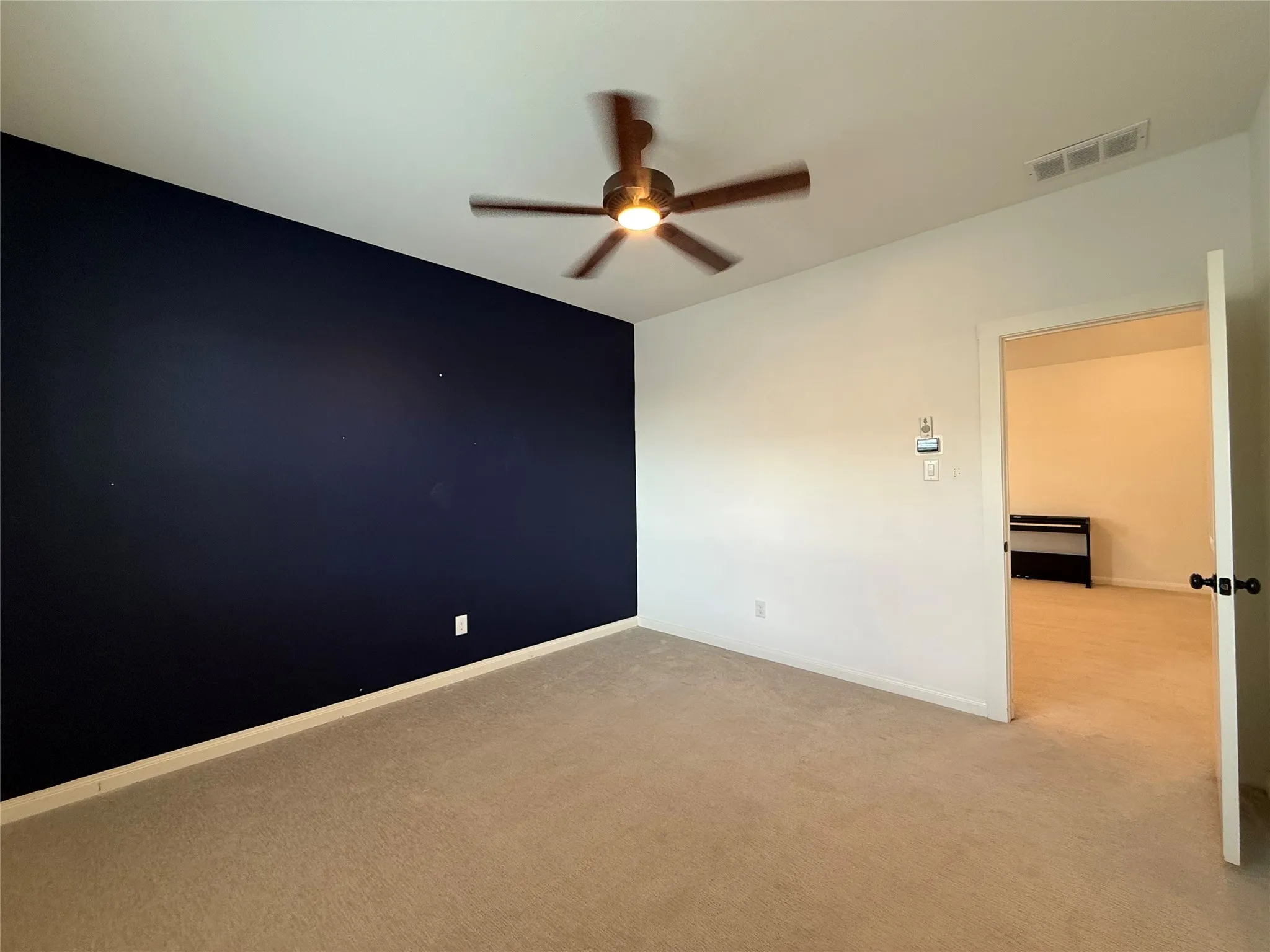 Room featuring a dark-toned accent wall, neutral carpeting, and a central ceiling fan with integrated lighting