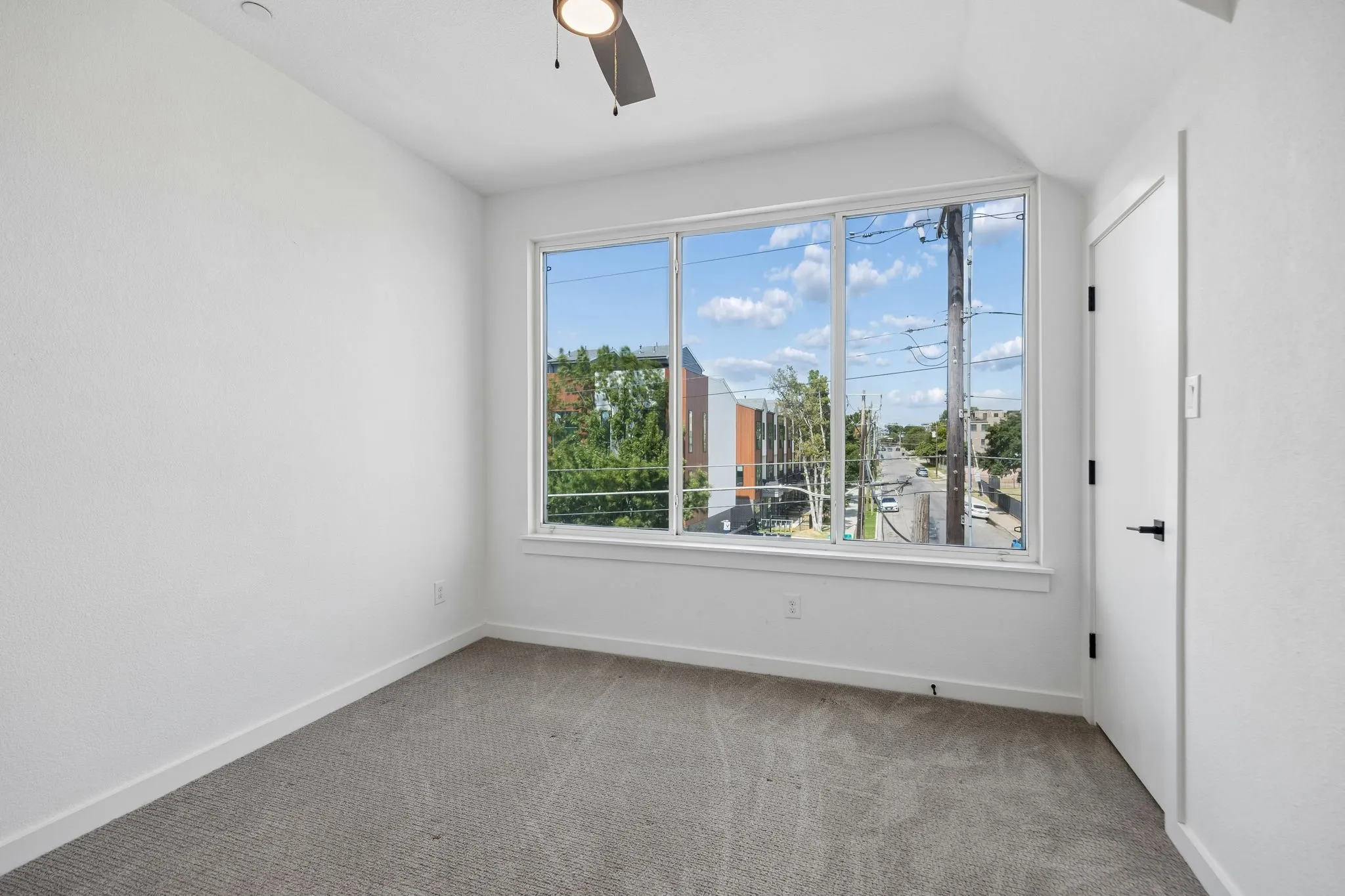 Neutral interior room featuring large picture windows, gray carpeting, a ceiling fan, and a single swing door with matte black hardware