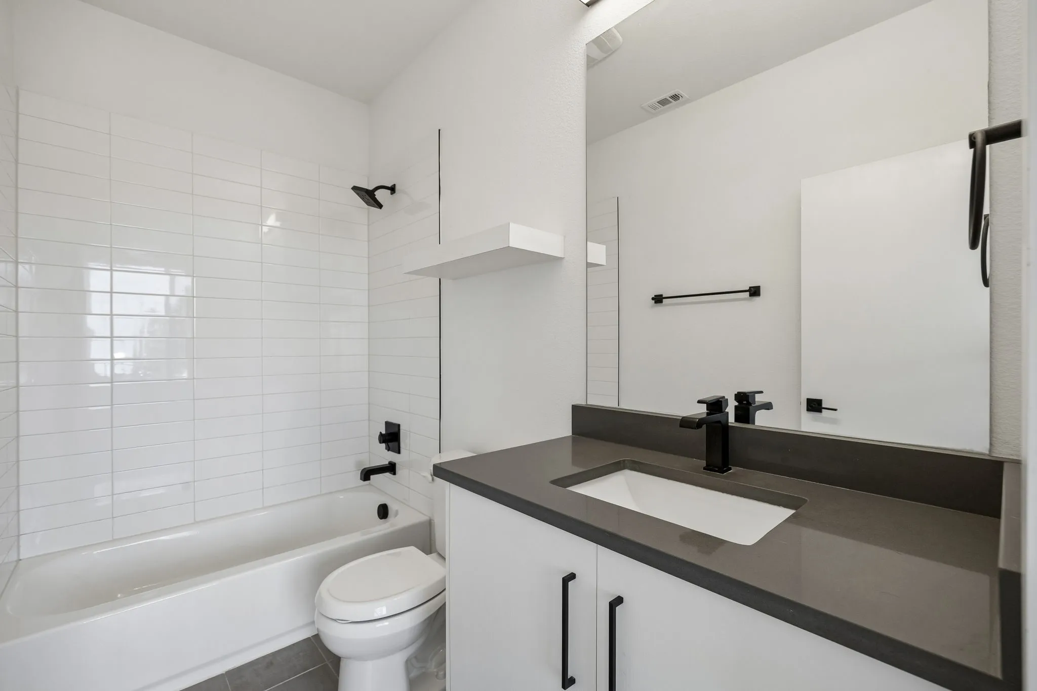 Bathroom featuring a white vanity with a dark gray countertop, undermount sink, matte black hardware, and a tub-shower combination with floor-to-ceiling white tile
