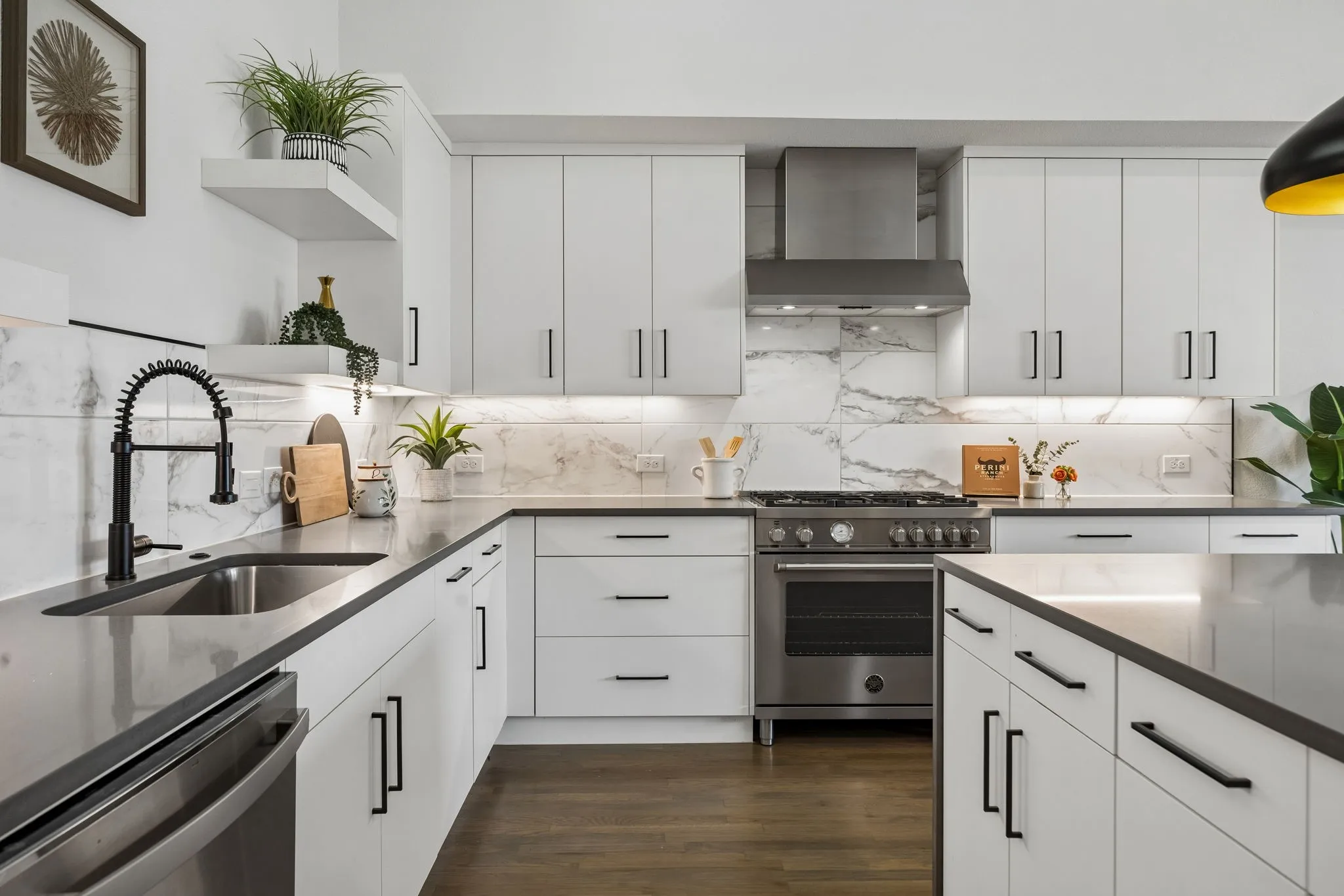 Kitchen featuring white flat-panel cabinetry, stone-finish countertops, full-height stone-patterned backsplash, stainless steel professional-style range with matching vent hood, and wood-finish flooring