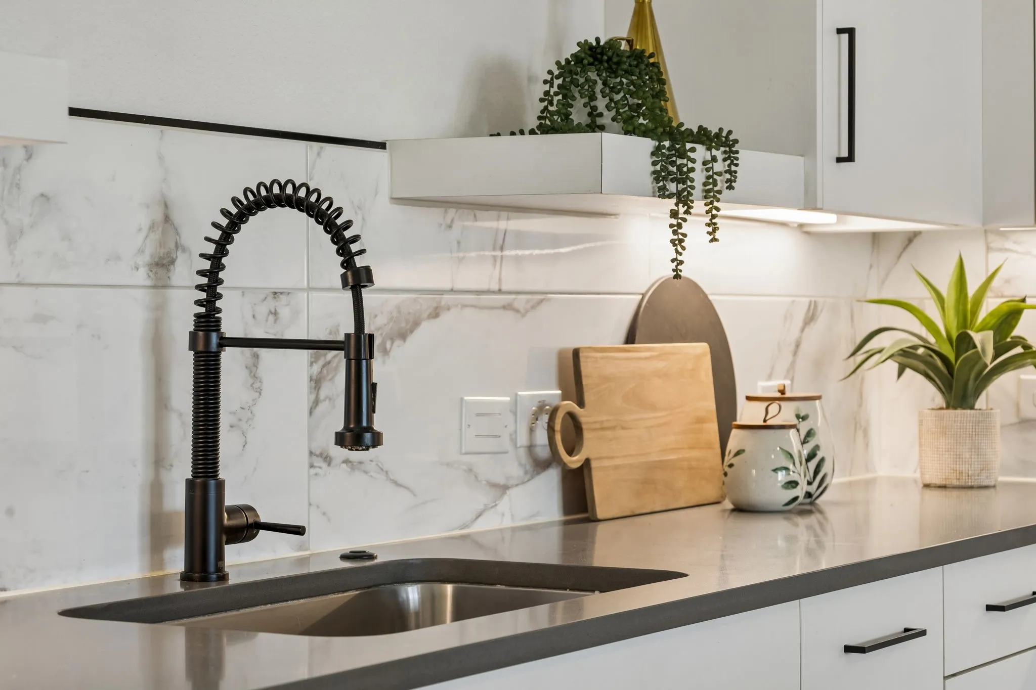 Kitchen featuring a matte black industrial-style spring faucet, undermount sink, solid surface countertop, white cabinetry with matte black hardware, and large-format tile backsplash