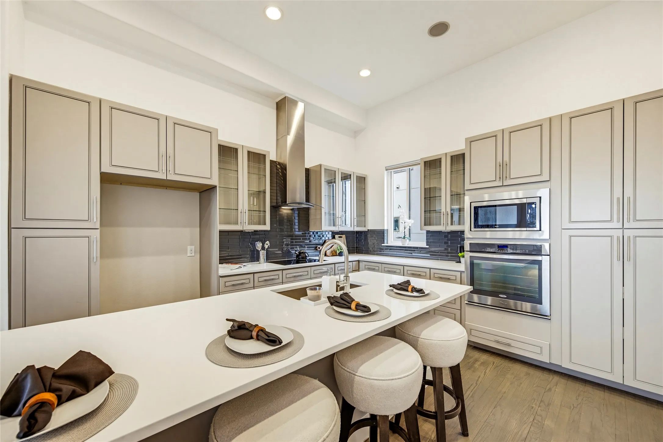 Kitchen featuring floor-to-ceiling cabinetry, a central island with a solid-surface countertop, stainless steel appliances, a chimney-style range hood, and wood-finish flooring