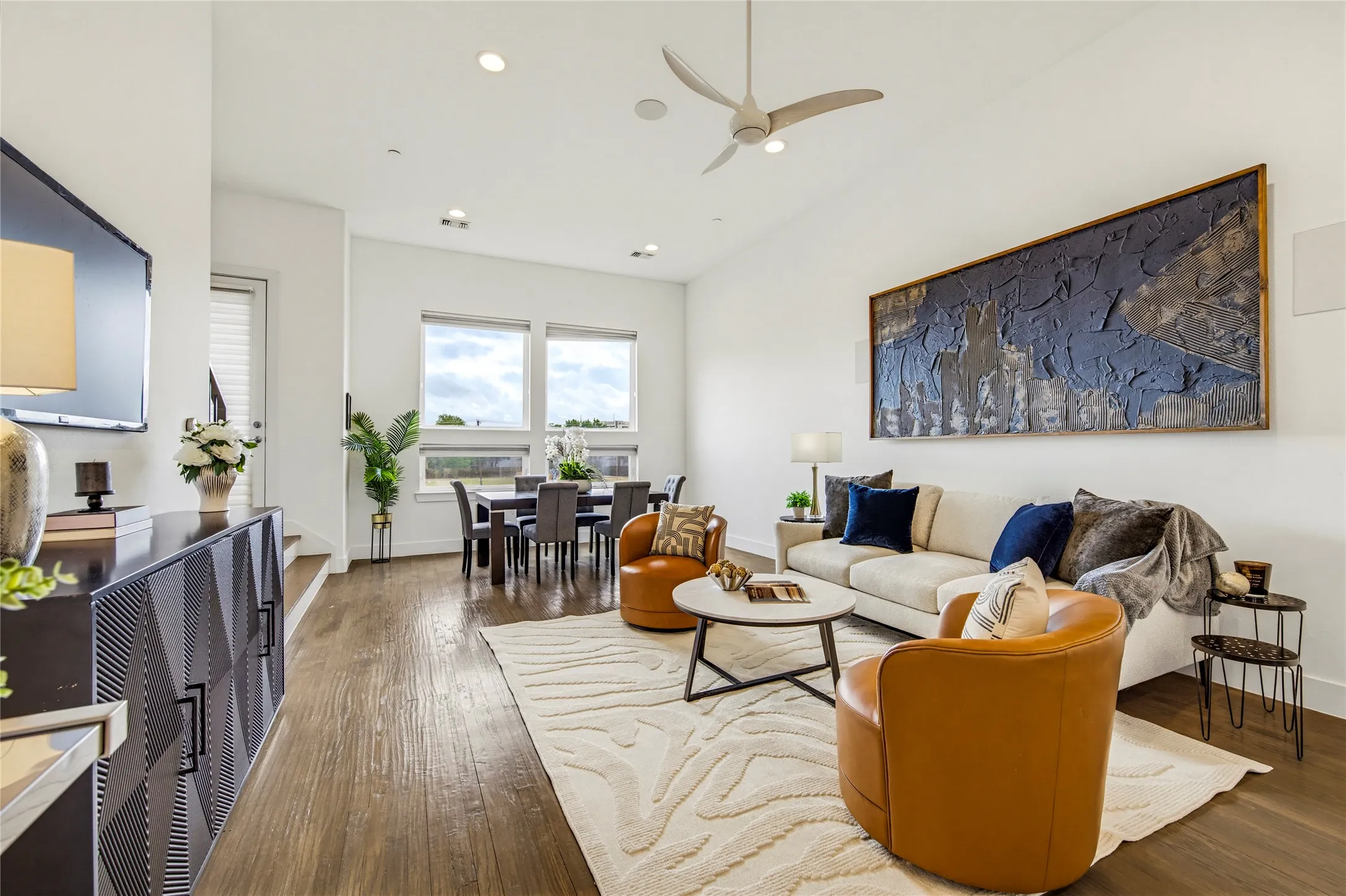 Living area featuring wood-finish flooring, high ceilings, recessed lighting, a modern ceiling fan, and large windows