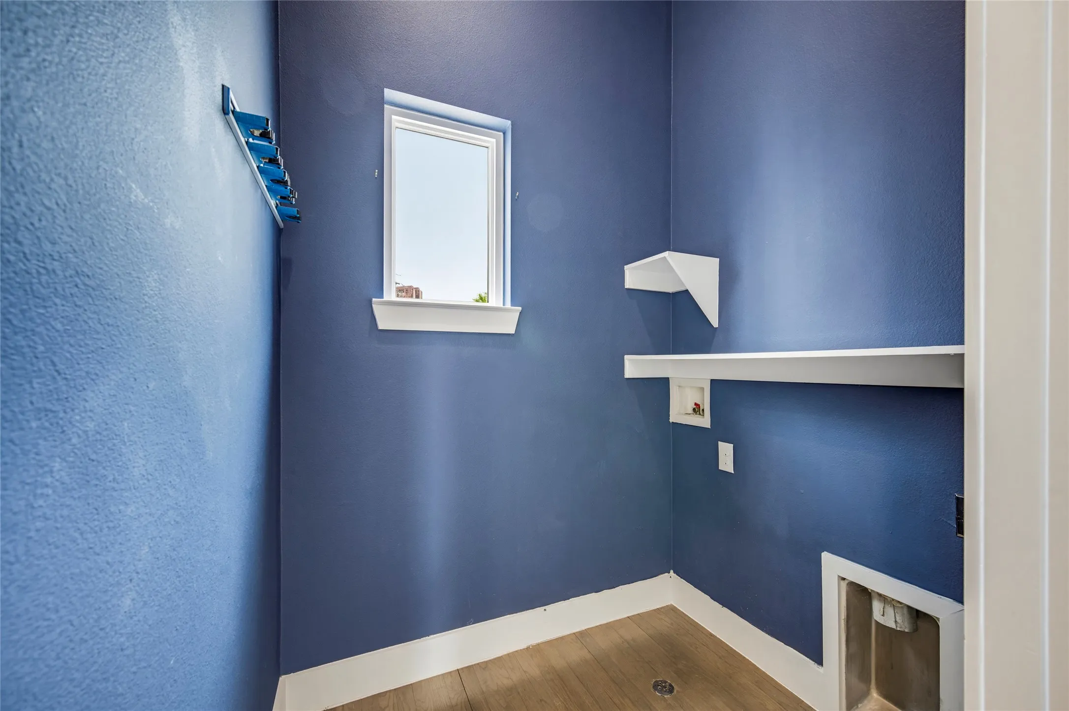 Utility space featuring wood-finish flooring, a single window, white built-in shelving, and dedicated hookups