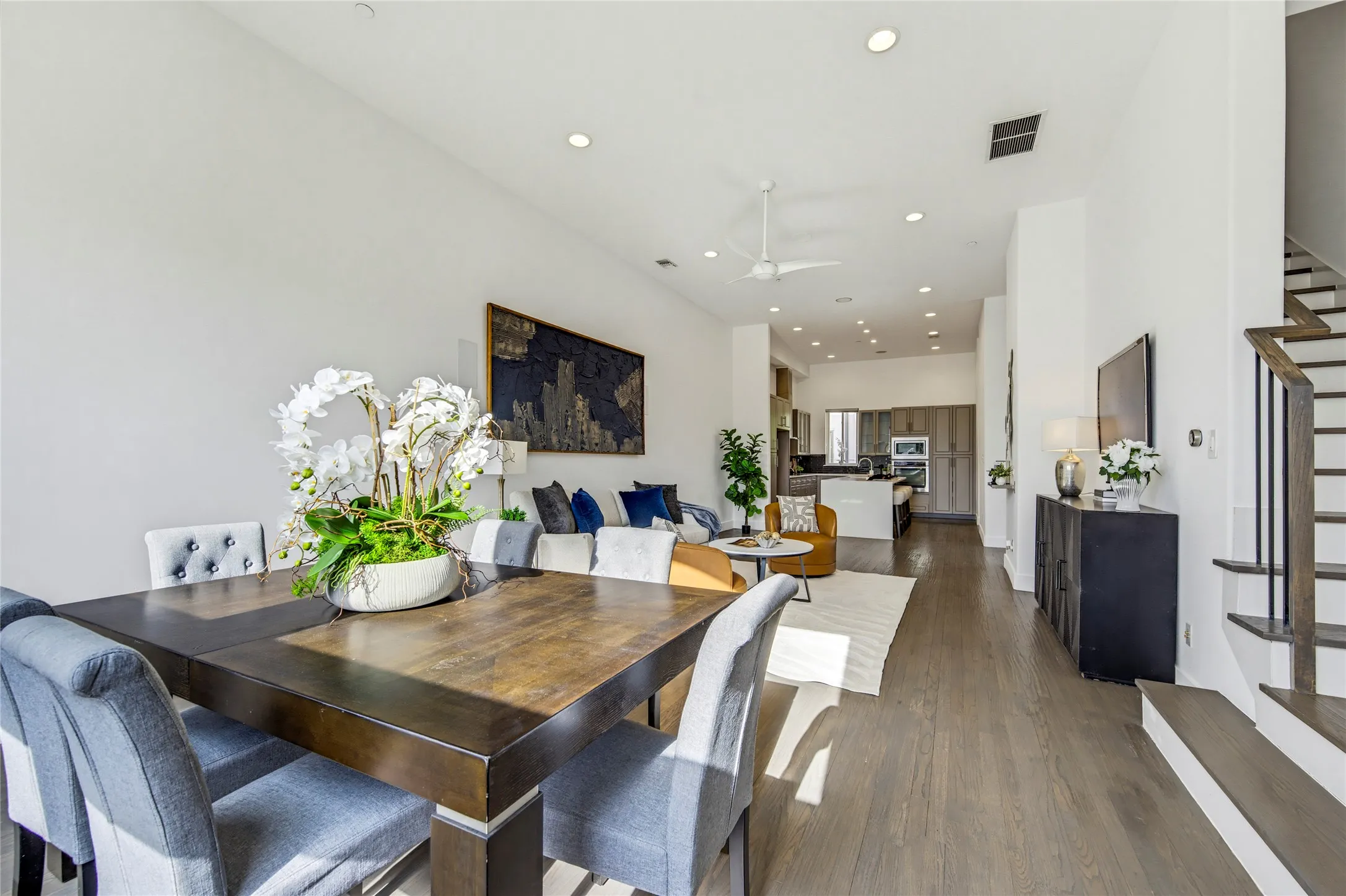 Open-concept floor plan with wood-finish flooring, recessed lighting, ceiling fan, and a staircase featuring dark metal railings