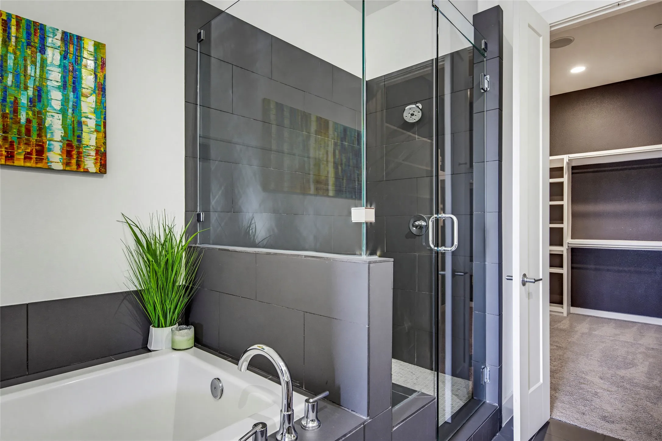 Deep soaking tub with chrome fixtures, glass-enclosed shower with large-format tile surround, and built-in closet shelving