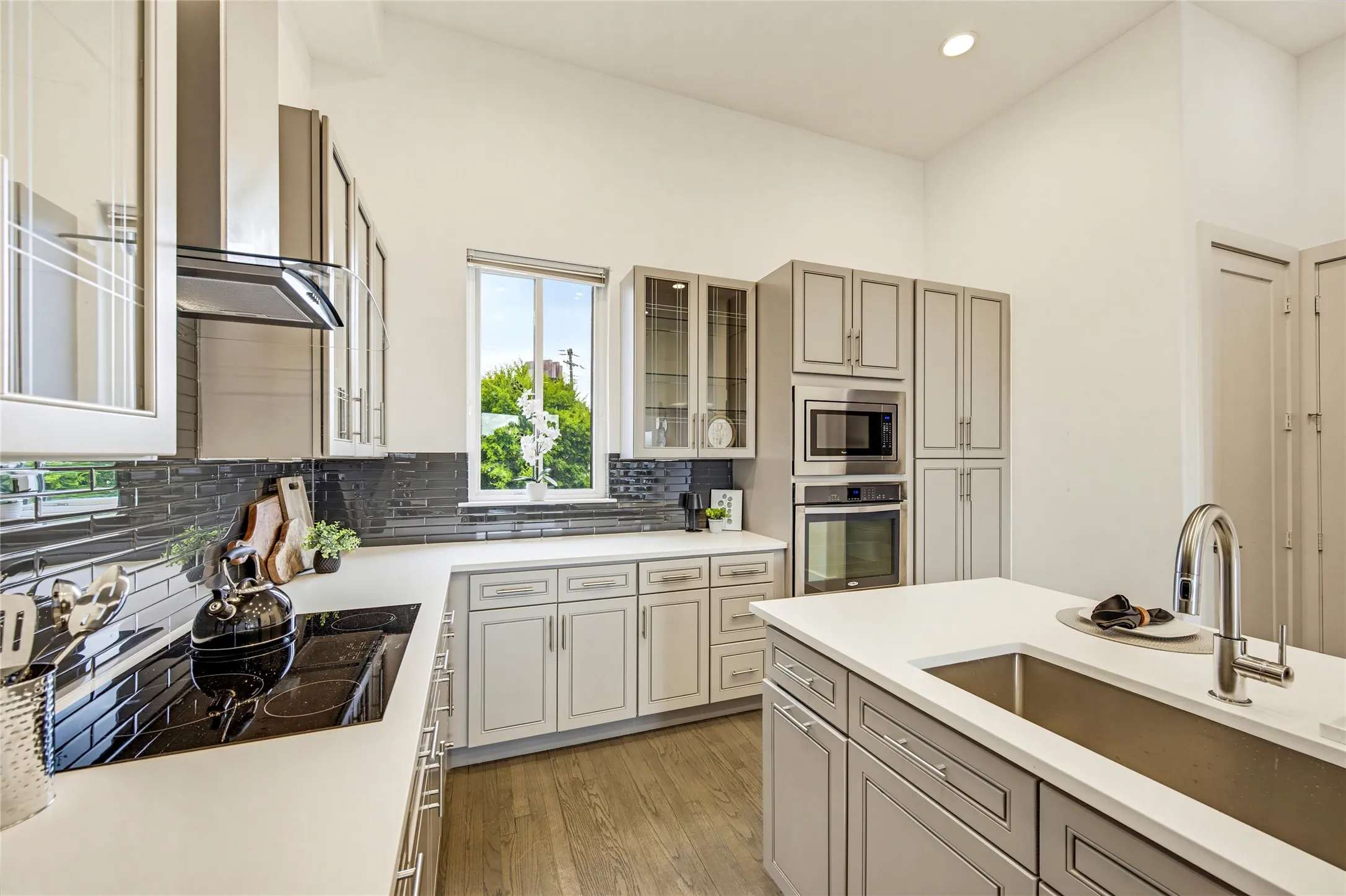 Kitchen featuring shaker-style cabinetry, white solid-surface countertops, horizontal tile backsplash, built-in stainless steel appliances, and wood-finish flooring