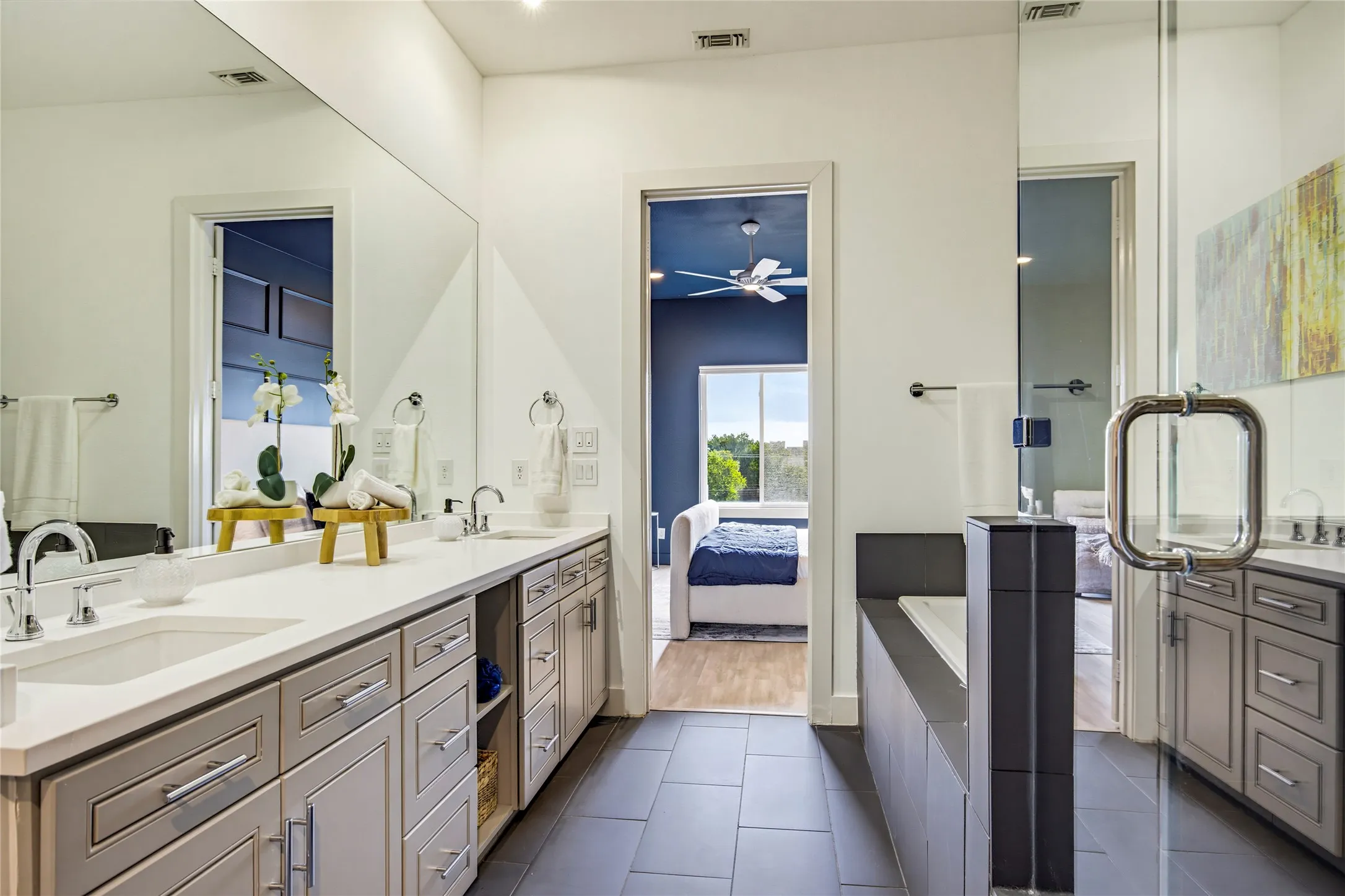 Bathroom featuring a long vanity with dual under-mount sinks, light-toned cabinetry, quartz countertops, a full-width wall mirror, and large-format floor tile