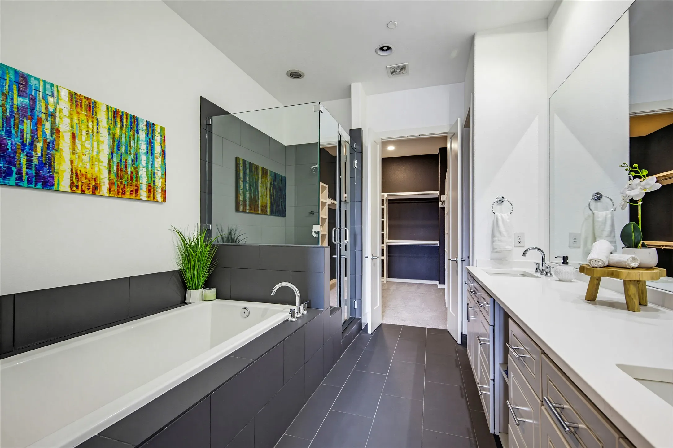 Bathroom featuring a dual-sink vanity with a quartz countertop, a deep soaking tub with tile surround, a glass-enclosed walk-in shower, and large-format tile flooring