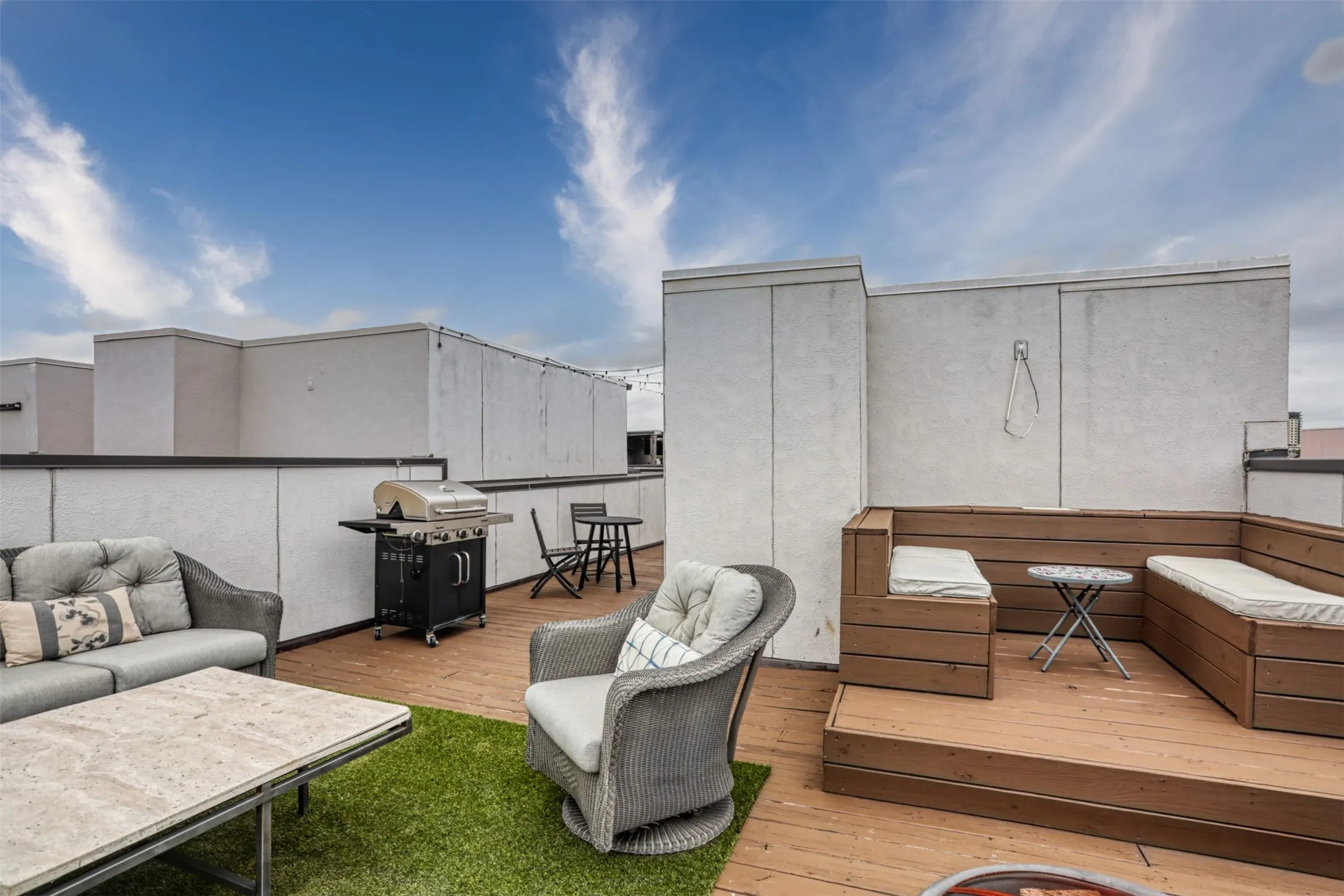 Rooftop terrace featuring wood-finish decking, built-in wooden bench seating, synthetic turf inlay, and high parapet walls