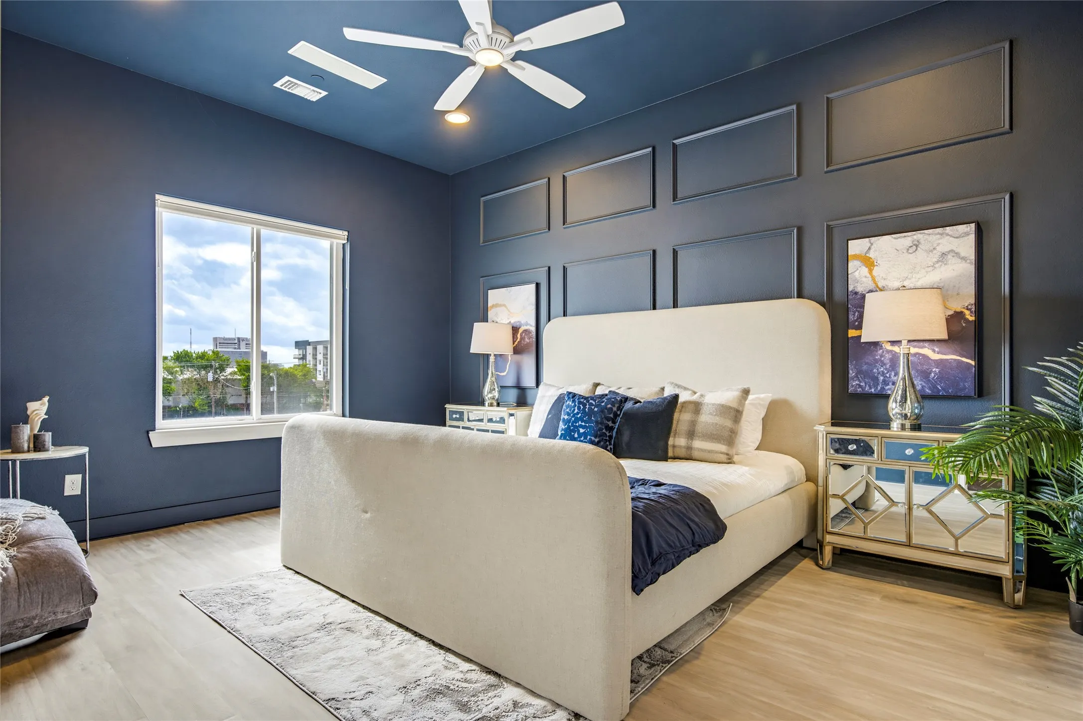 Room featuring deep-toned wall paint, decorative wall molding, light-toned wood-finish flooring, and a ceiling fan with integrated lighting