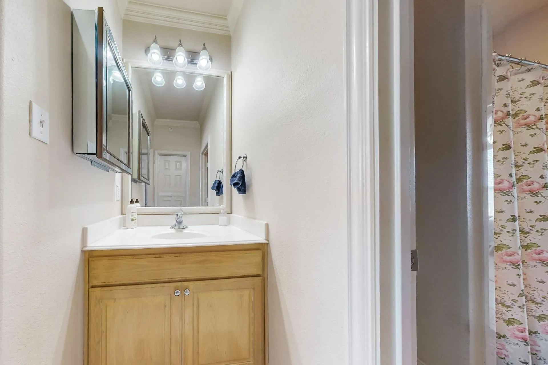Bathroom featuring a light wood vanity with a white countertop, integrated sink, framed vanity mirror, three-light fixture, and recessed medicine cabinet