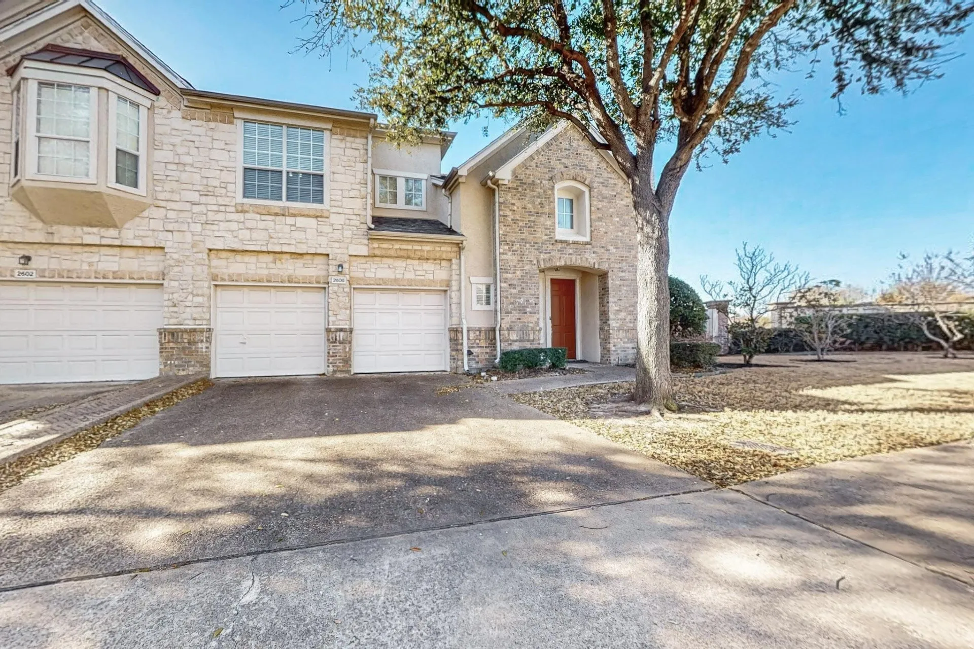 Multi-unit exterior featuring a textured stone facade, bay window, two attached garage bays, and a concrete driveway