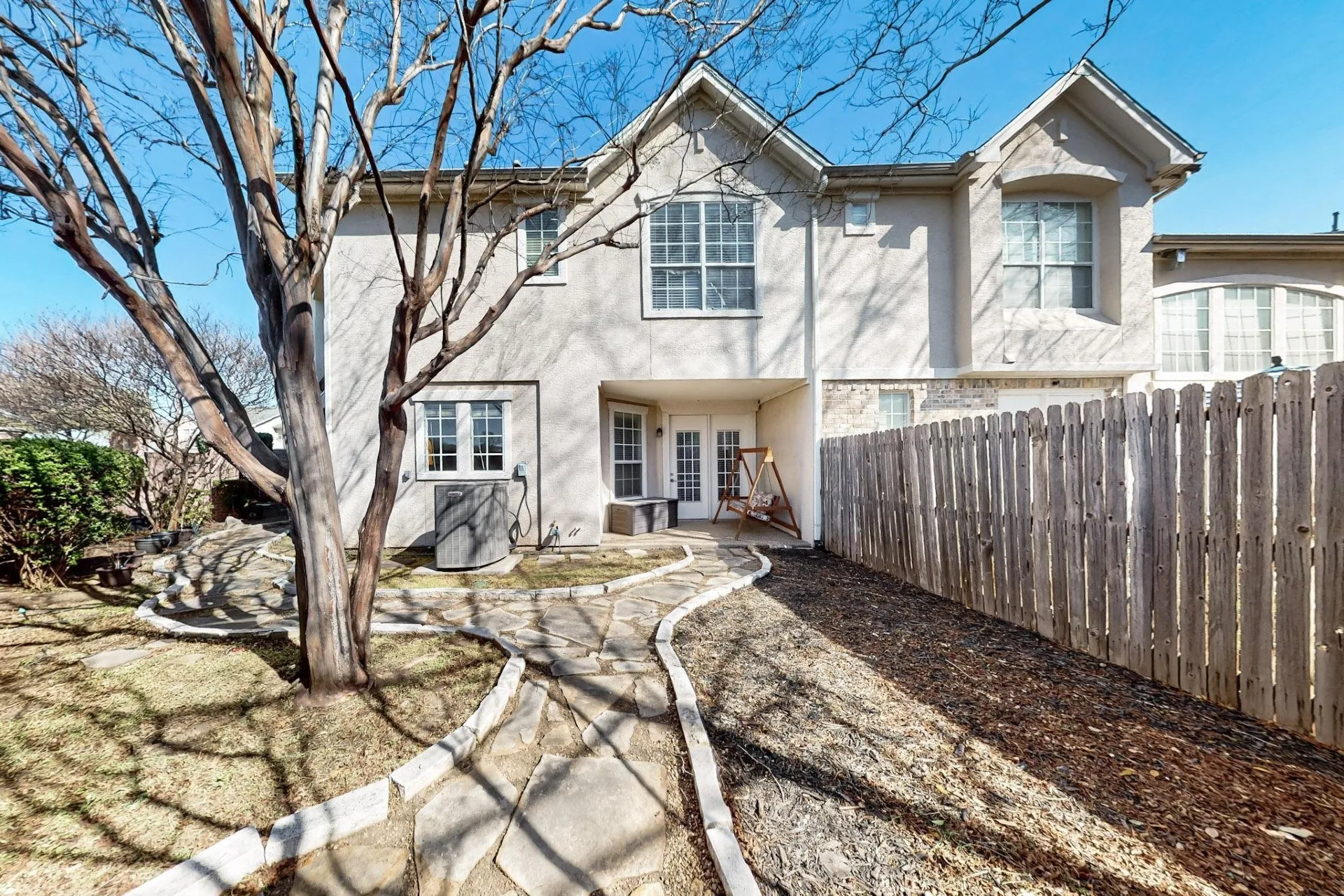 Rear exterior featuring stucco siding, multi-gabled roofline, irregular stone pathway, and wood privacy fencing