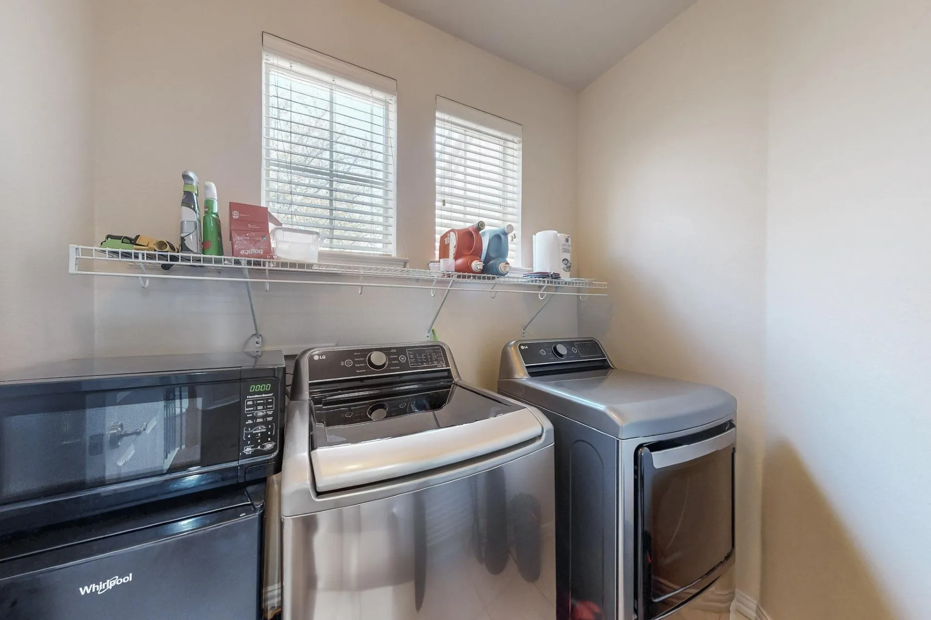 Laundry area featuring two windows with horizontal blinds and an installed wire shelving unit