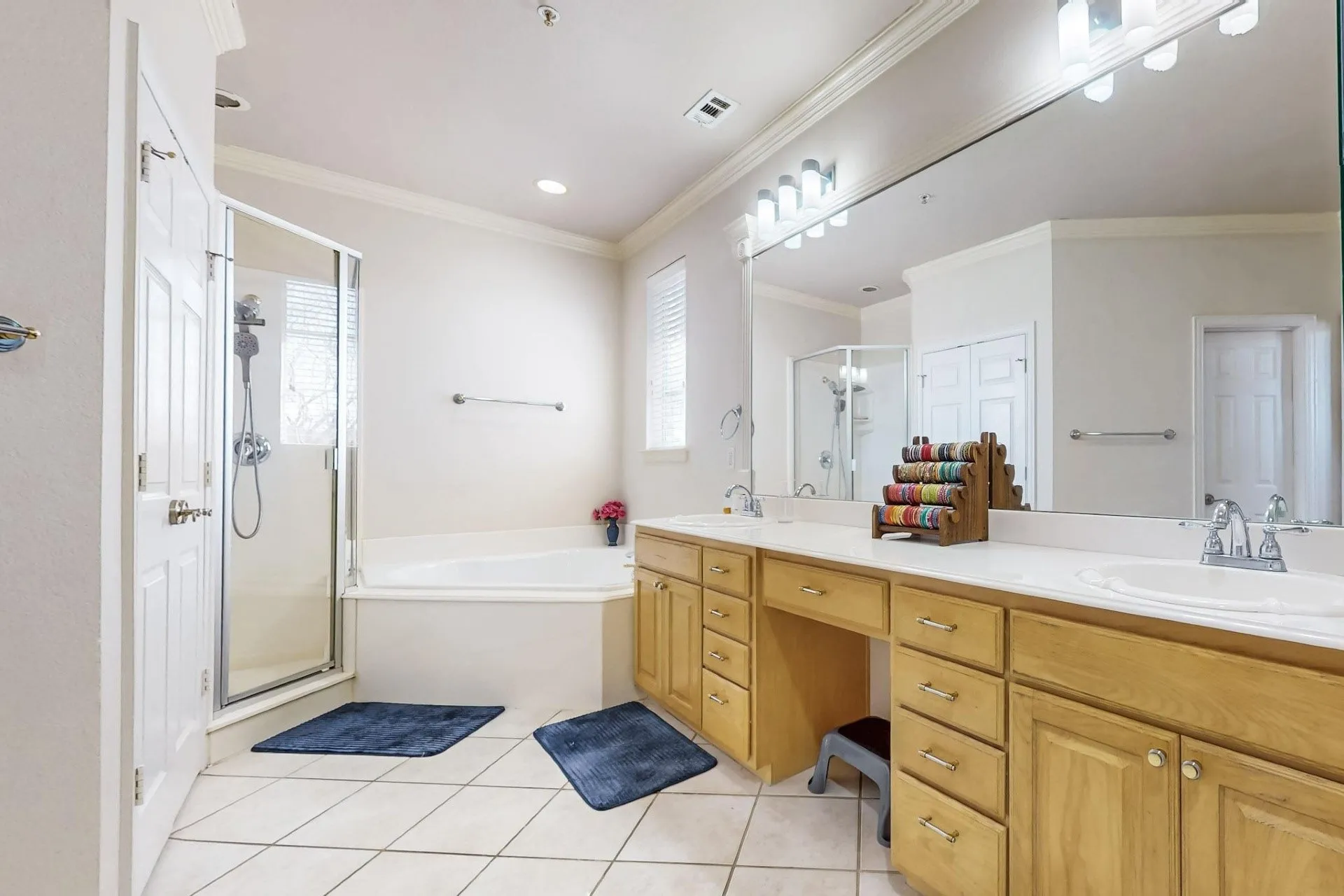 Bathroom featuring a soaking tub, a separate glass-enclosed shower, light wood cabinetry, a dual-sink vanity with a solid-surface countertop, and ceramic tile flooring