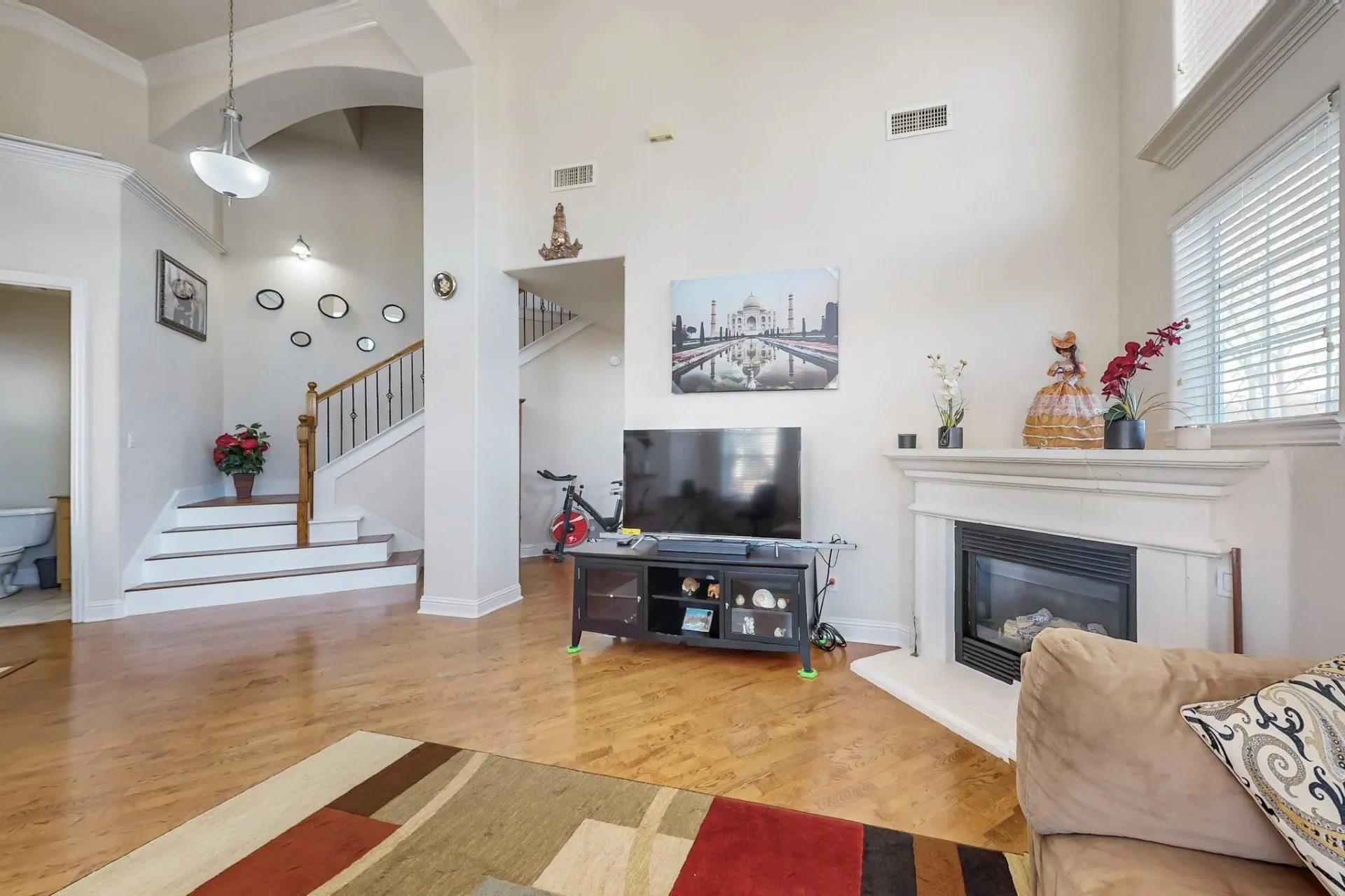 High ceilings featuring architectural archways, wood-finish flooring, a fireplace with a decorative mantel, and a staircase with a wooden handrail and metal balusters