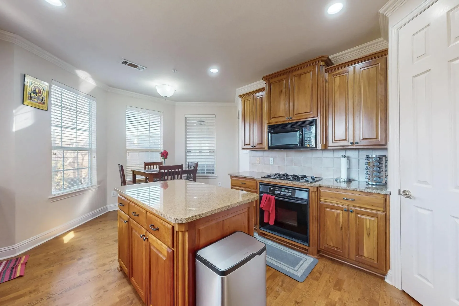 Kitchen featuring wood cabinetry, stone countertops, central island, gas cooktop, and wood-finish flooring