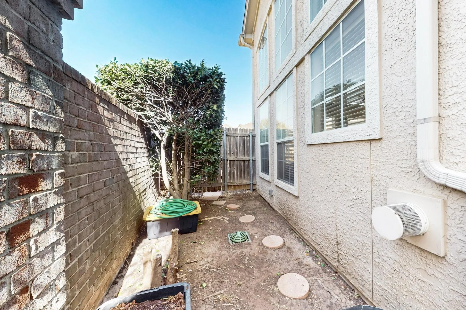 Exterior side yard featuring a brick retaining wall, stucco siding, and multi-pane windows
