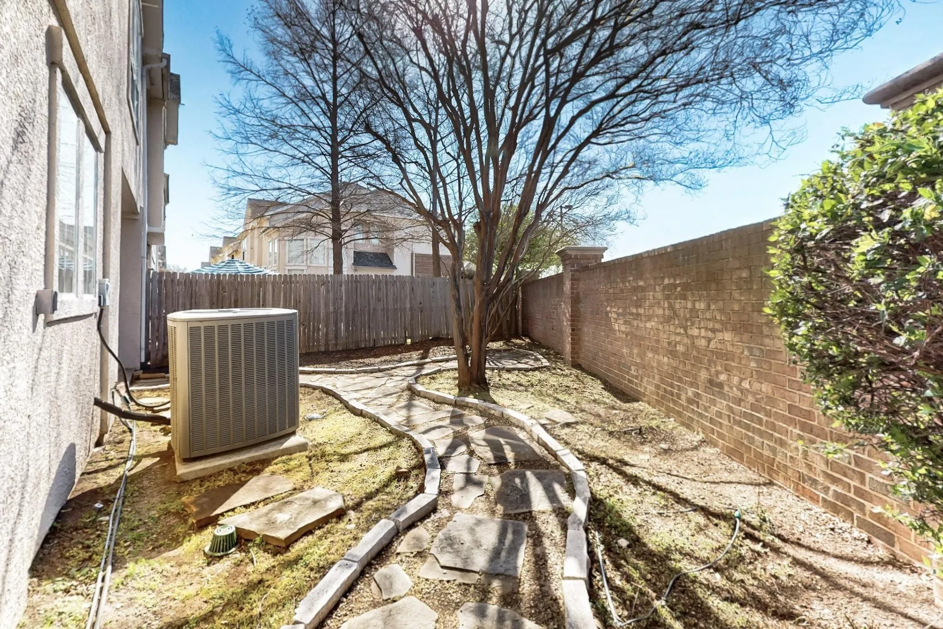 Side yard featuring a stone pathway, mature tree, brick perimeter wall, and wood-panel fencing