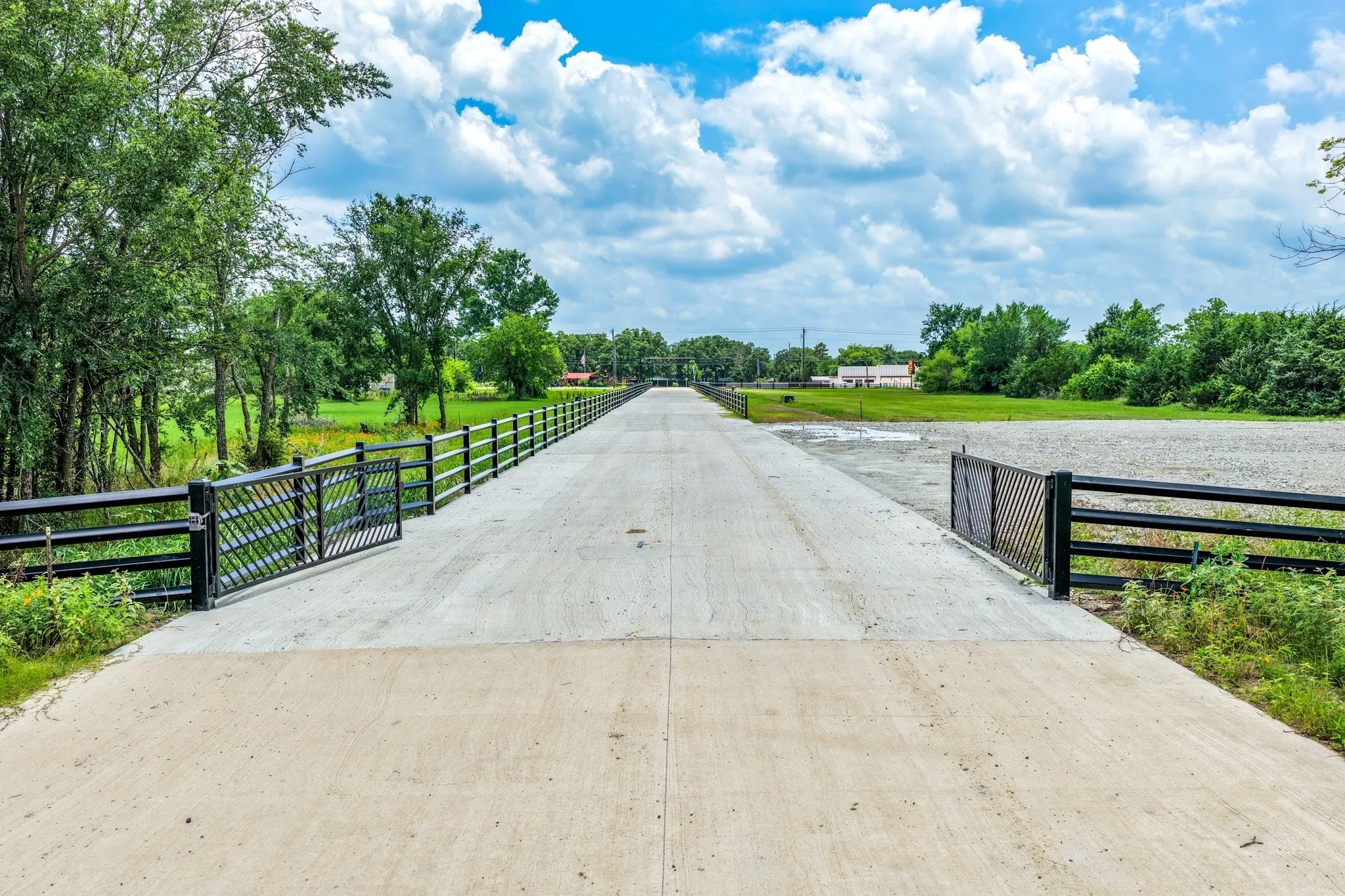 Concrete driveway featuring metal fencing, gated entry, and expansive surrounding acreage