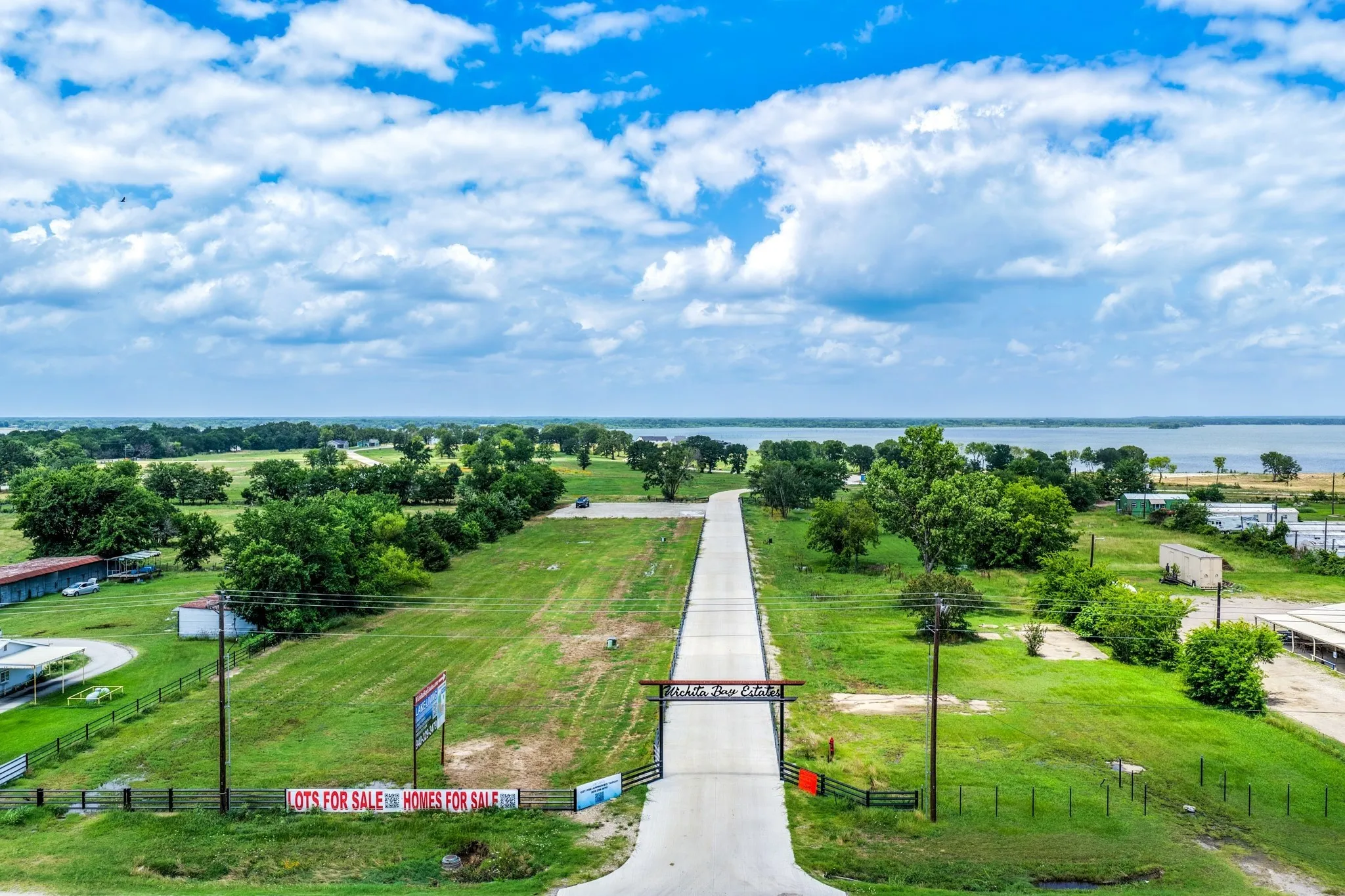 Expansive land parcel featuring a paved thoroughfare, gated entry archway, and mature tree clusters
