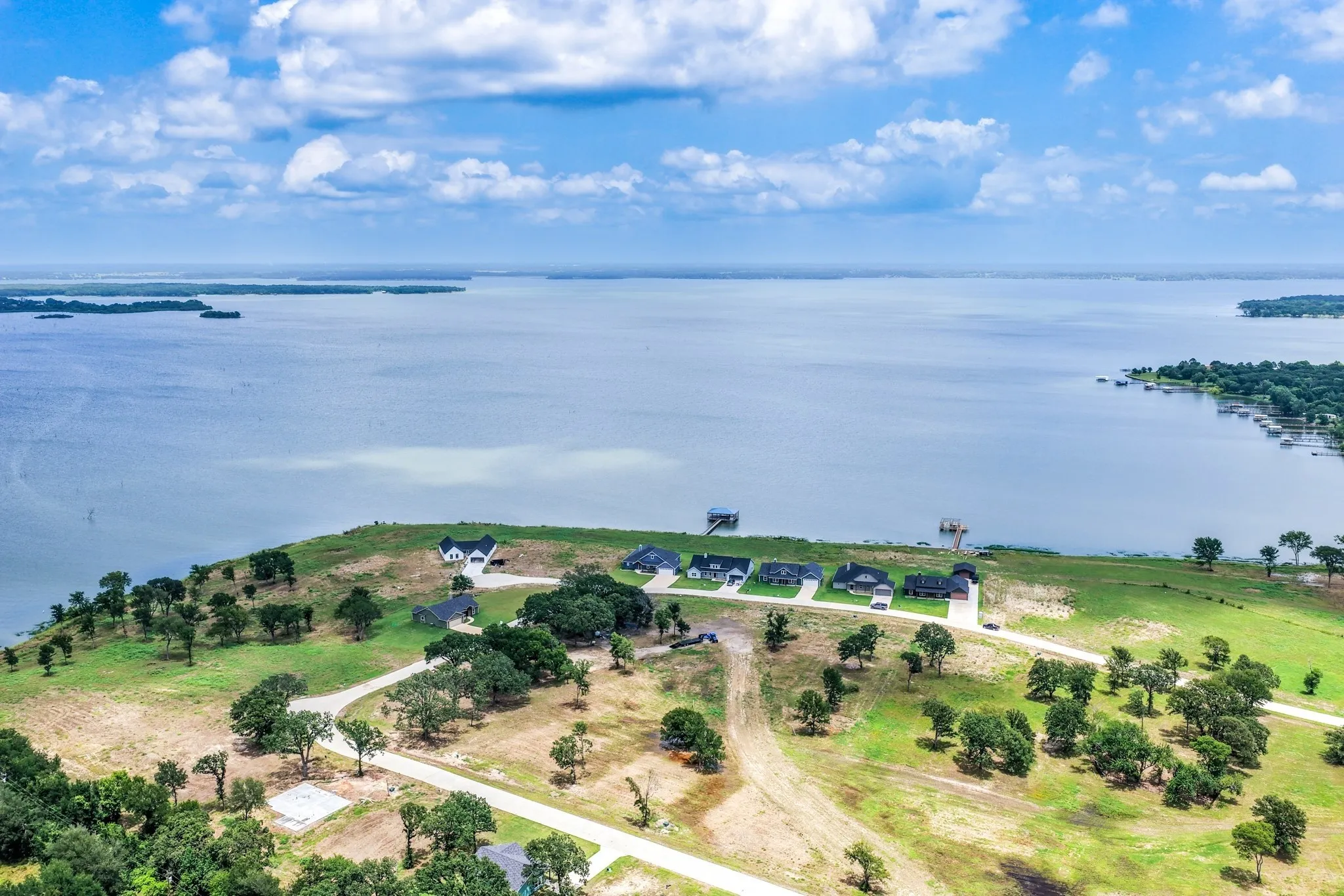 Aerial perspective of waterfront acreage featuring expansive shoreline, mature oak trees, paved access roads, and multiple residential structures