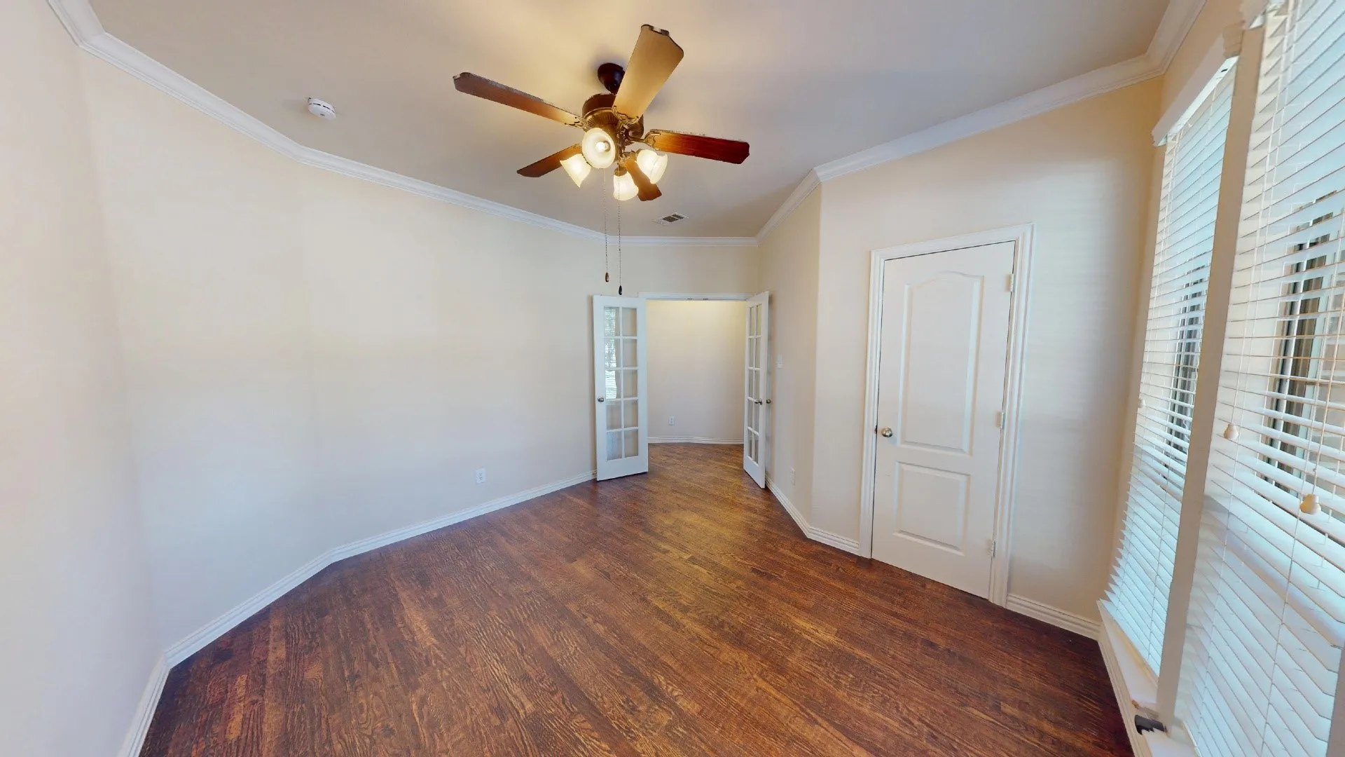 Wood-finish flooring, multi-pane glass French doors, crown molding, and a ceiling-mounted light fixture with a central fan