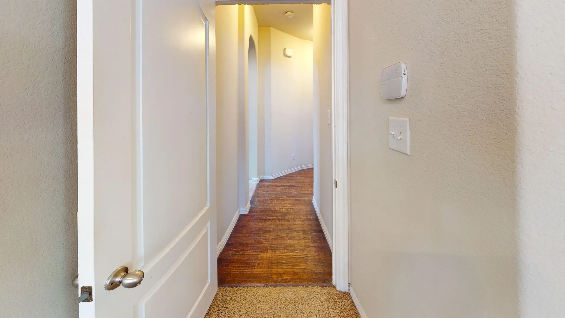 Hallway featuring wood-finish flooring, a neutral wall palette, arched architectural detailing, and a wall-mounted security panel