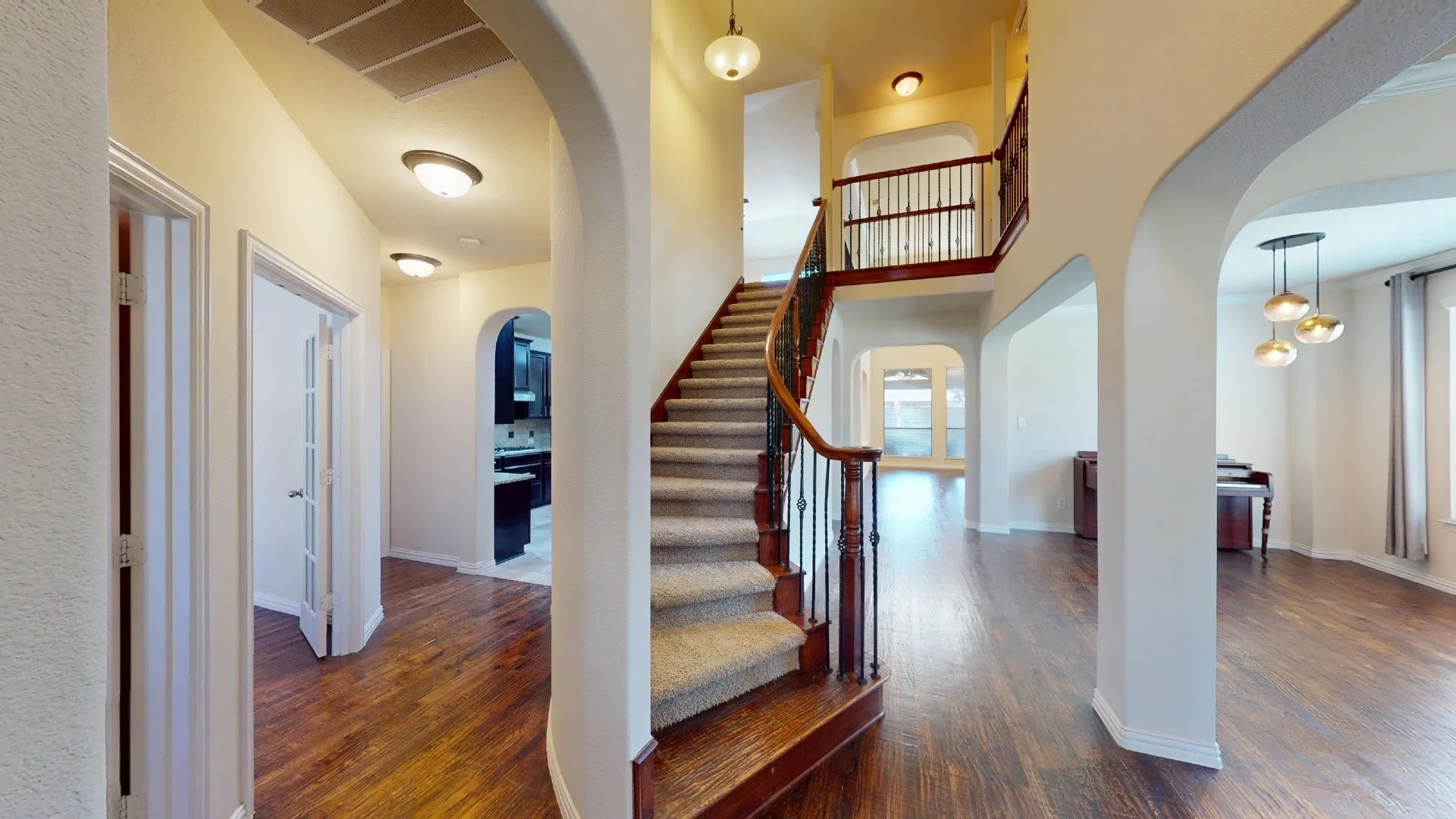 Foyer featuring arched structural openings, wood-finish flooring, a carpeted staircase with decorative metal balusters, and a tiered chandelier