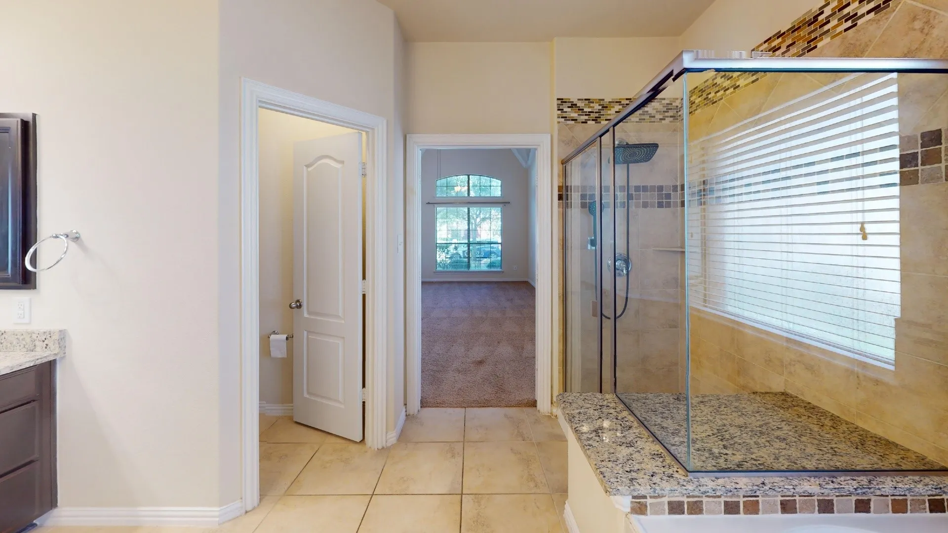Bathroom featuring large-format floor tiling, a glass-enclosed shower with mosaic tile accents, stone-top vanity, and arched window detailing