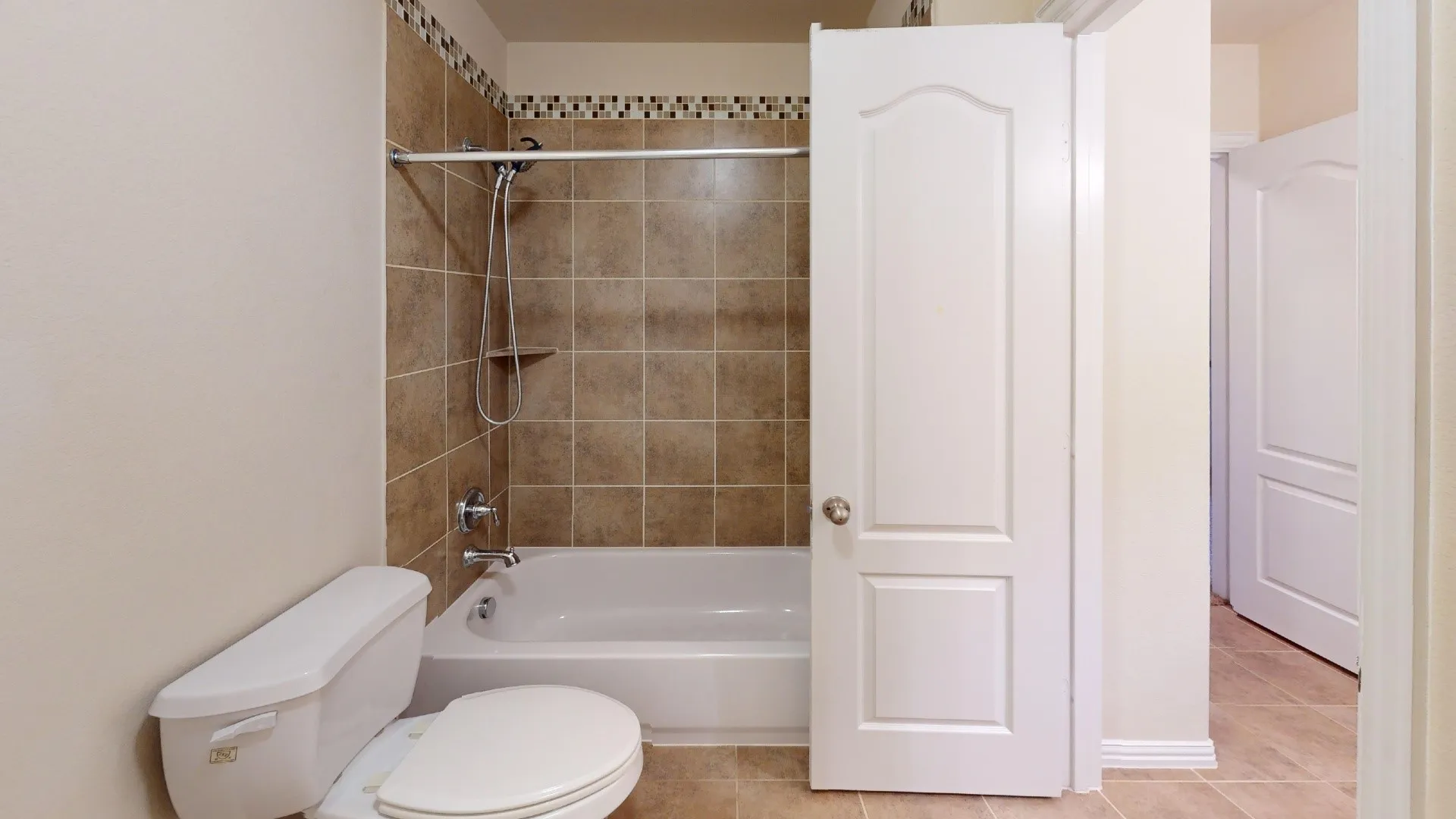 Bathroom featuring a porcelain tub with tile surround, decorative mosaic tile accent border, wall-mounted shower head, and tile flooring