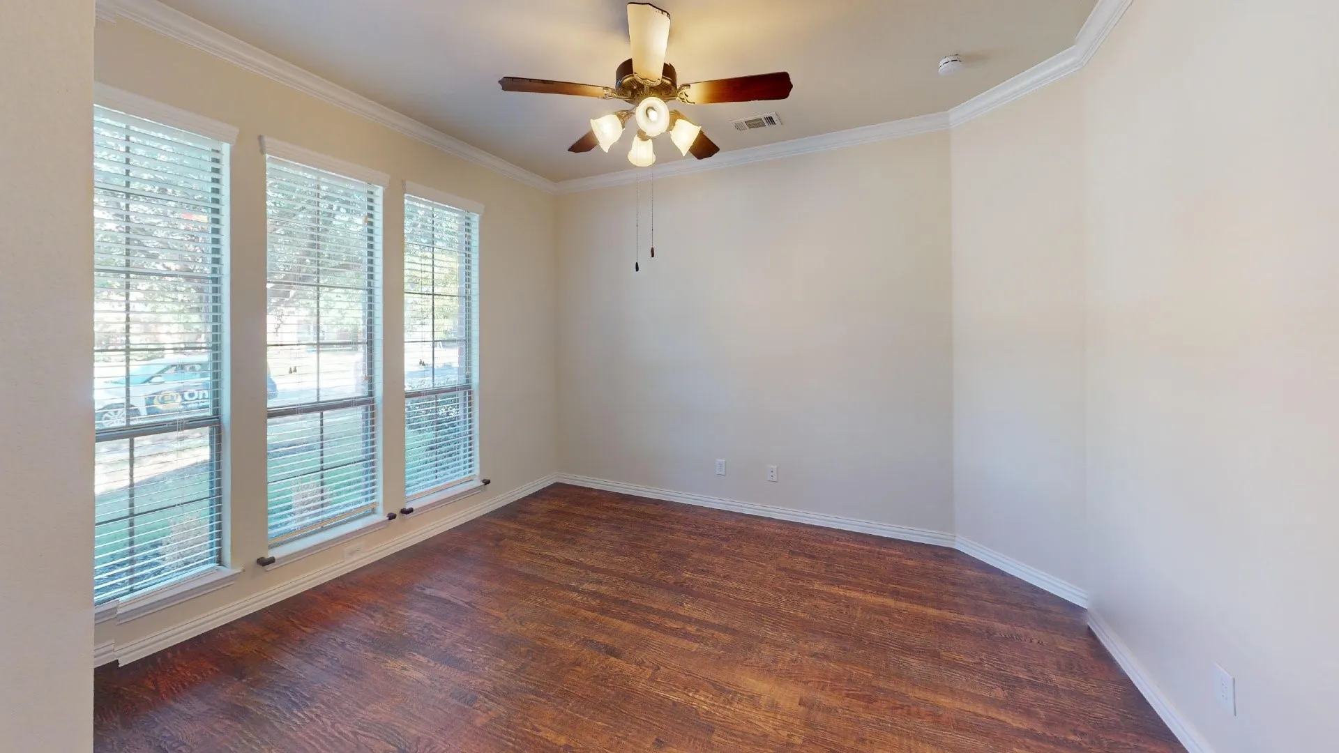 Room featuring wood-finish flooring, three windows with grid panes, crown molding, and a multi-light ceiling fan