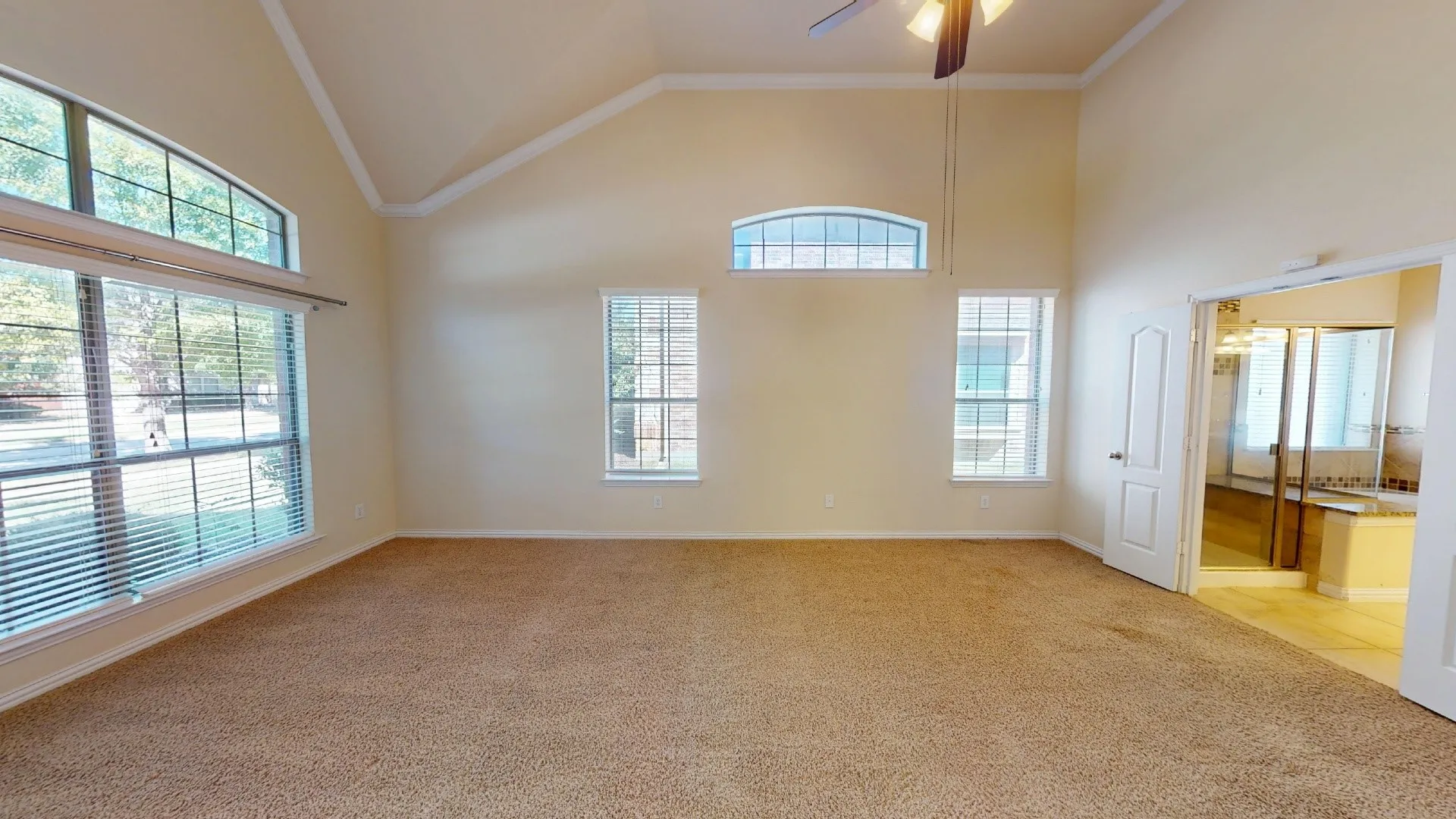 Vaulted ceiling featuring a central lighted ceiling fan, expansive windows with arched transom accents, and neutral wall-to-wall carpeting