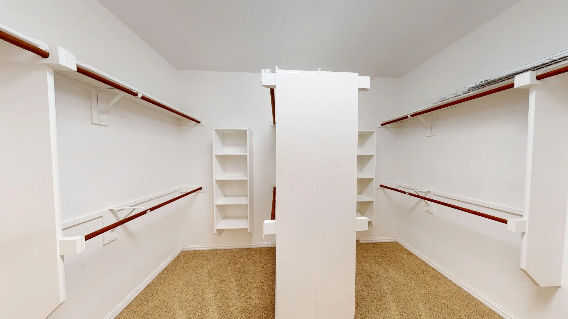 Walk-in storage space featuring custom white shelving, integrated hanging rods, a central divider partition, and wall-to-wall carpeting