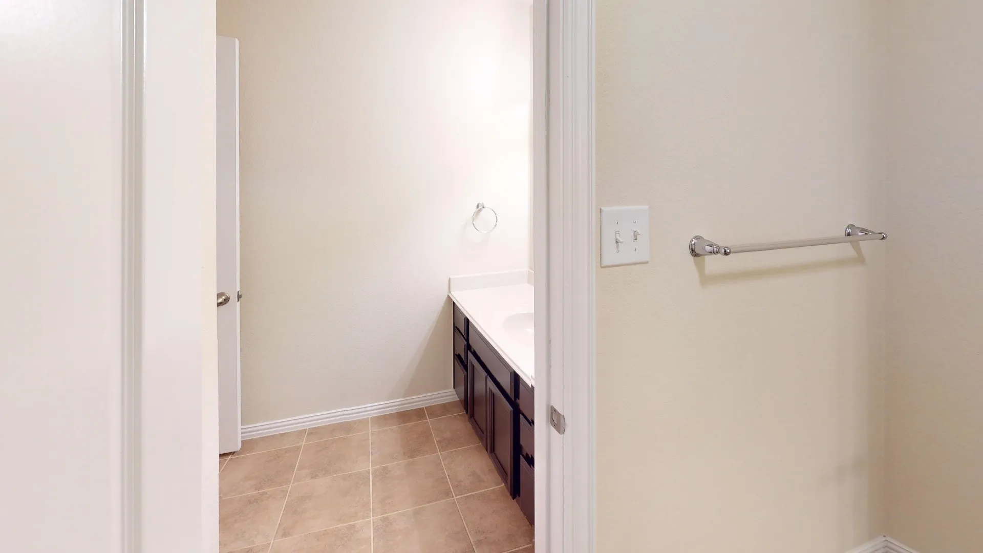 Bathroom featuring tile flooring, a dark-finish vanity cabinet with a solid-surface countertop, an integrated sink, and polished chrome hardware