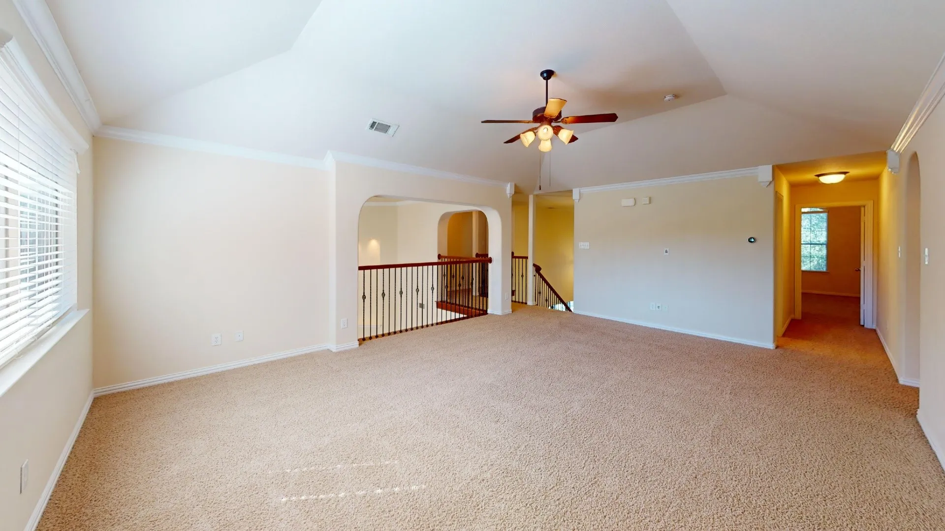 Vaulted ceiling featuring a central lighted ceiling fan, arched wall openings, metal spindle railing, and neutral wall-to-wall carpeting