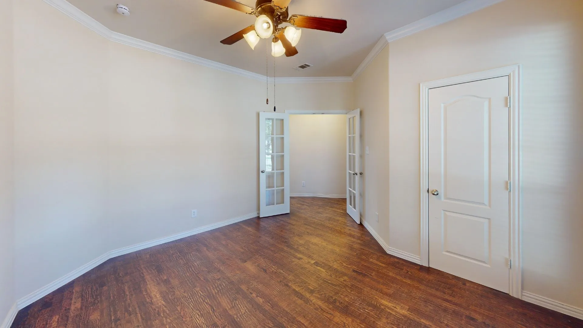 Wood-finish flooring, crown molding, ceiling fan with light fixture, arched-panel interior door, and French-style doors