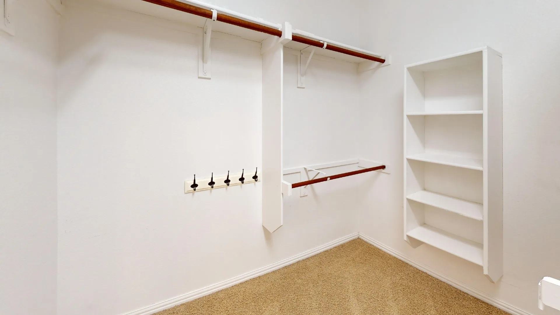 Walk-in closet featuring multi-level hanging rods, built-in shelving unit, wall-mounted hook rack, and neutral carpeting