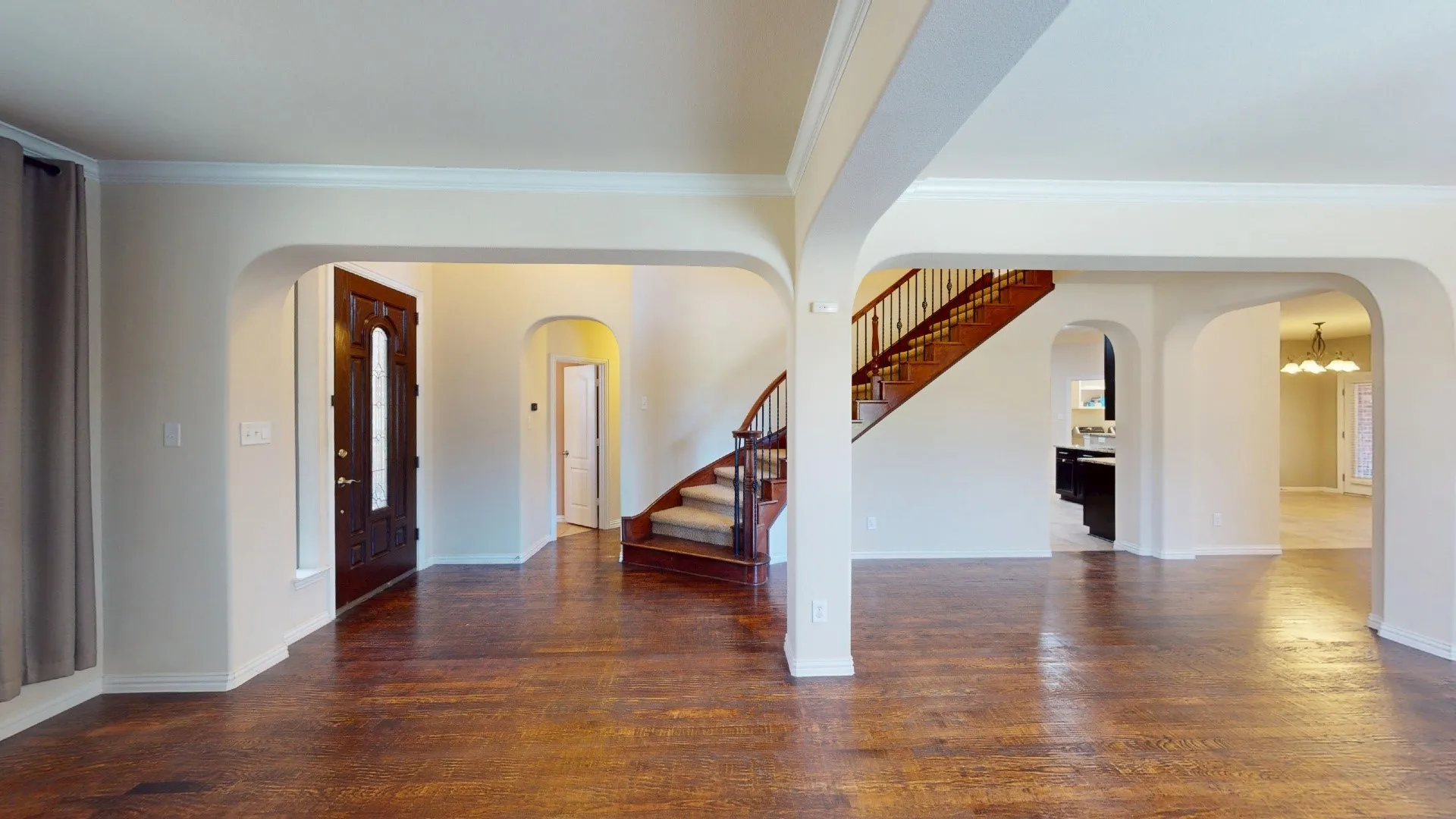 Open interior featuring wood-finish flooring, prominent arched doorways, and a wood staircase with a metal railing