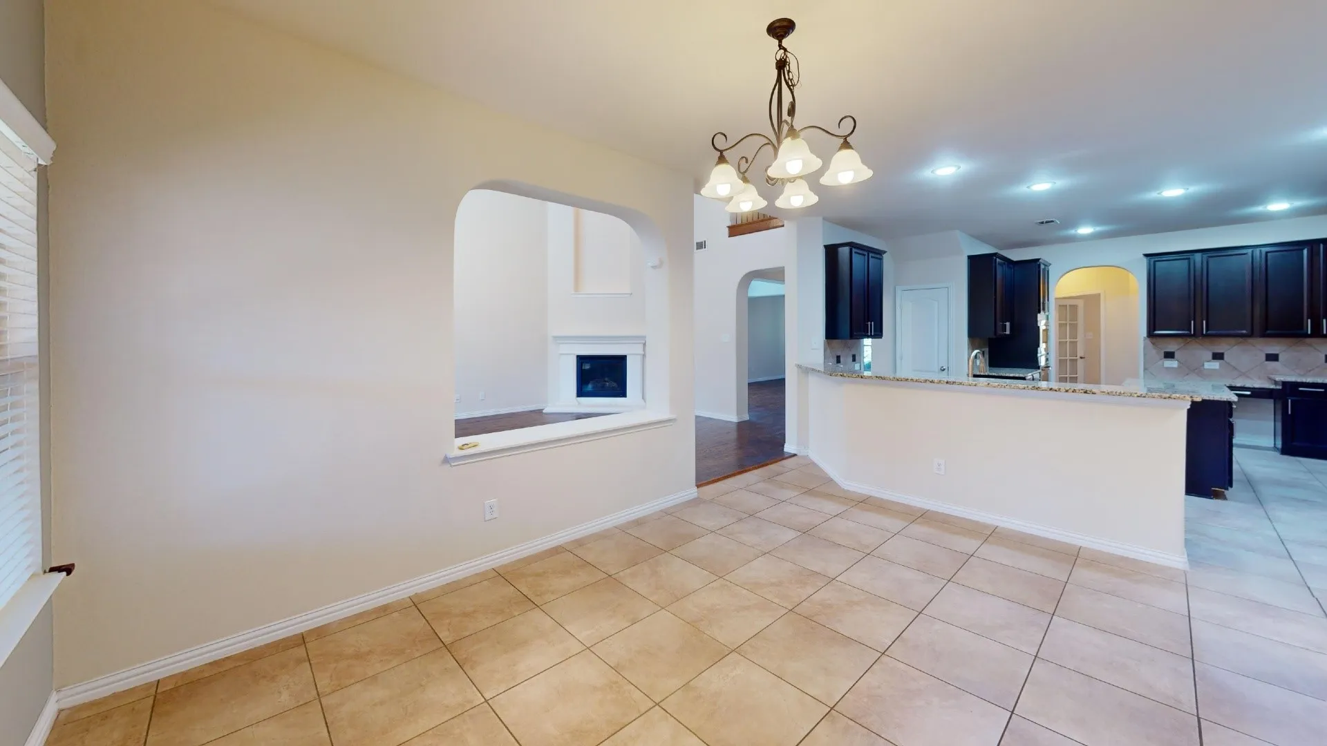 Ceramic tile flooring, arched wall pass-through, dark-toned cabinetry, stone-finish countertops, and multi-bulb chandelier