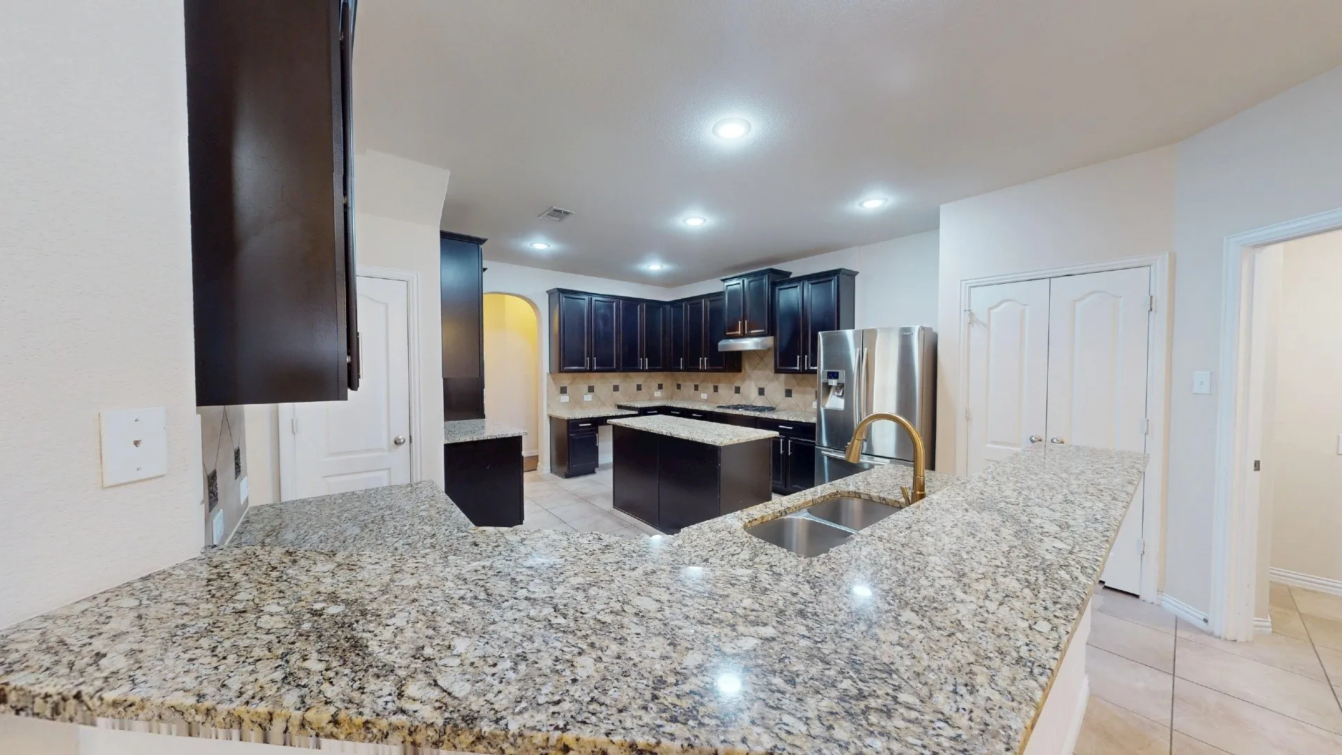 Kitchen featuring dark cabinetry, stone countertops, a center island, dual-basin stainless steel sink, and stainless steel appliances