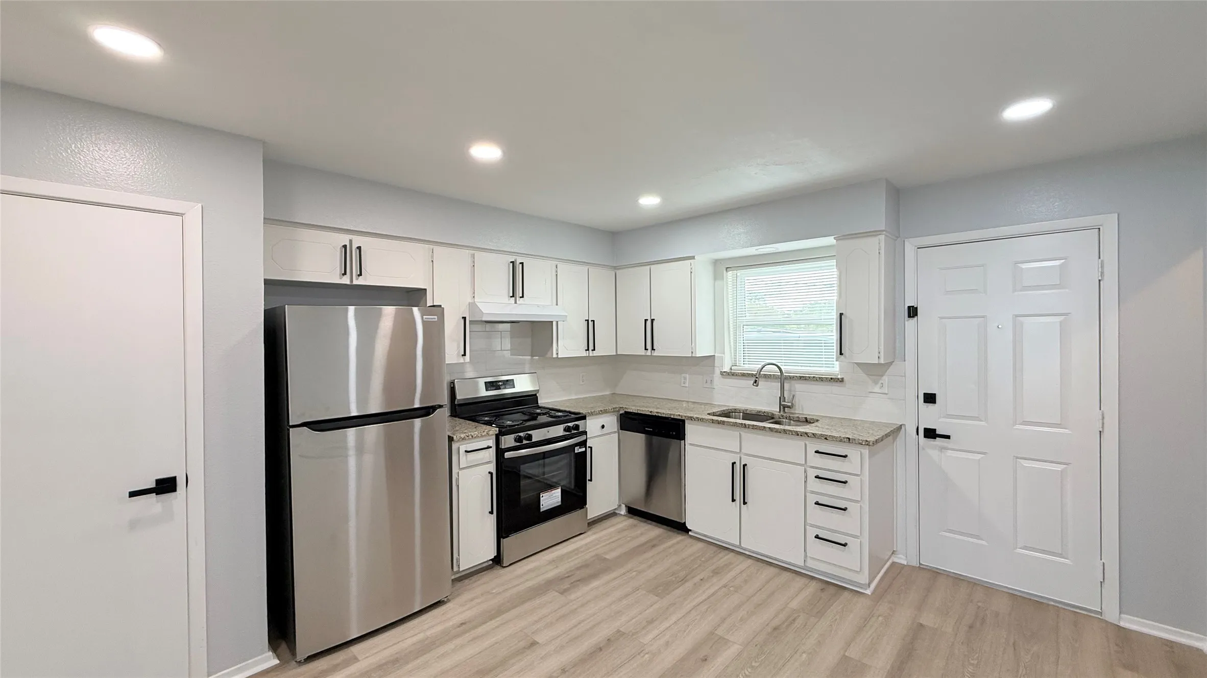 Kitchen featuring white shaker cabinetry, stone-finish countertops, stainless steel appliances, matte black hardware, and wood-finish flooring