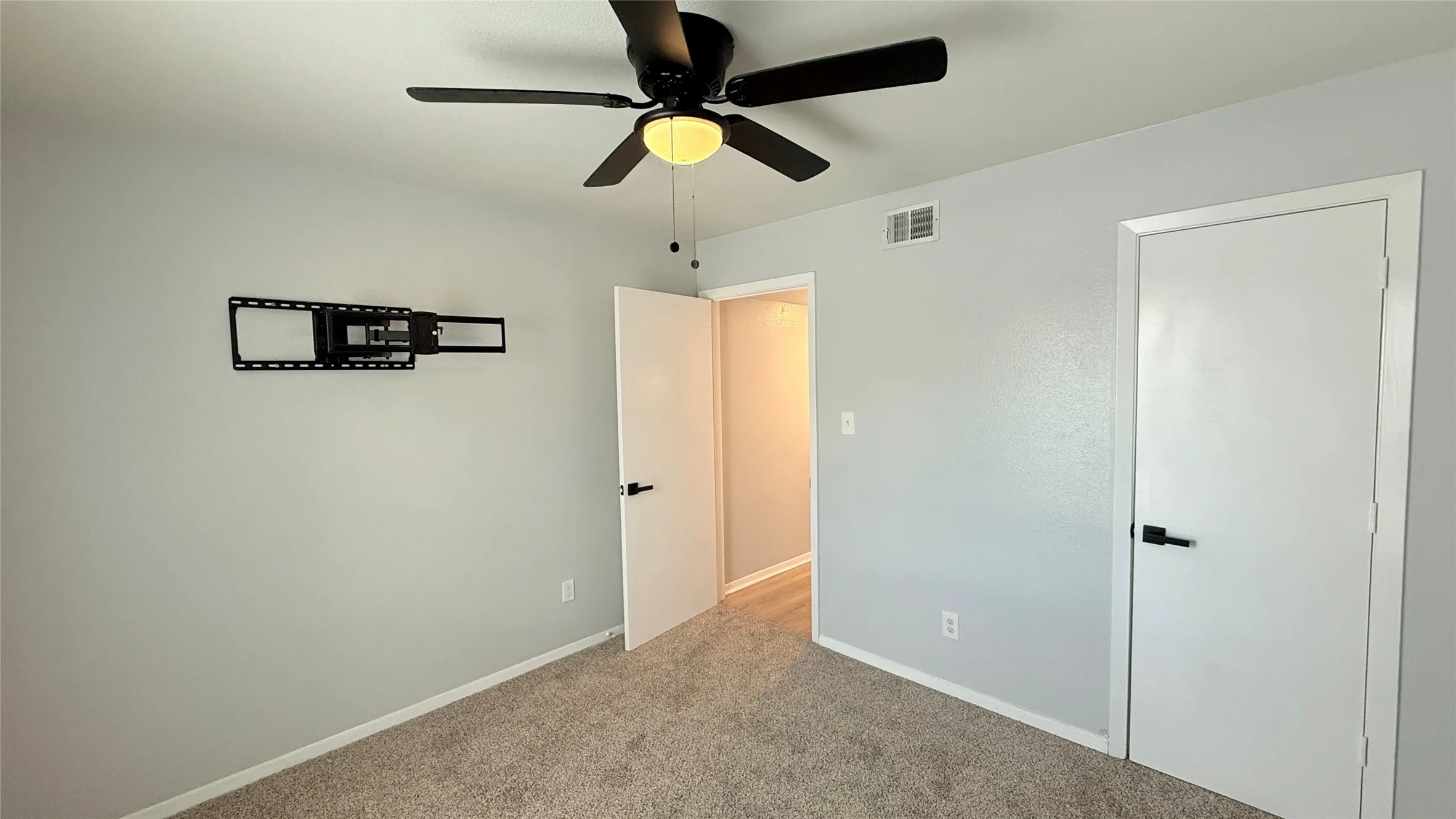 Neutral-toned interior featuring wall-to-wall carpeting, a matte black ceiling fan with integrated lighting, and minimalist interior doors with matte black hardware