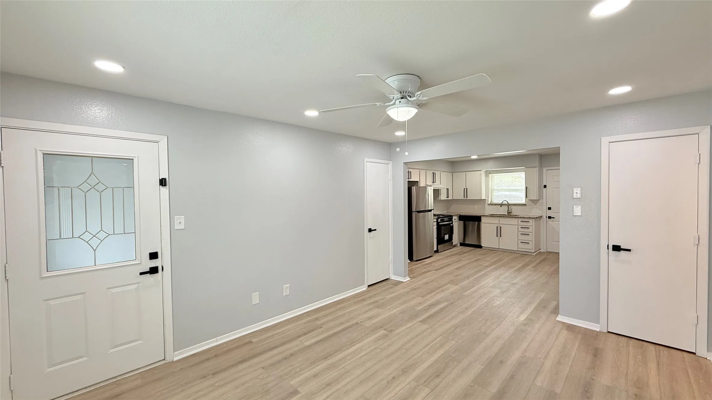 Interior featuring wood-finish flooring, recessed lighting, a ceiling fan with integrated light fixture, an exterior entry door with a decorative glass panel, and kitchen cabinetry with stainless steel appliances